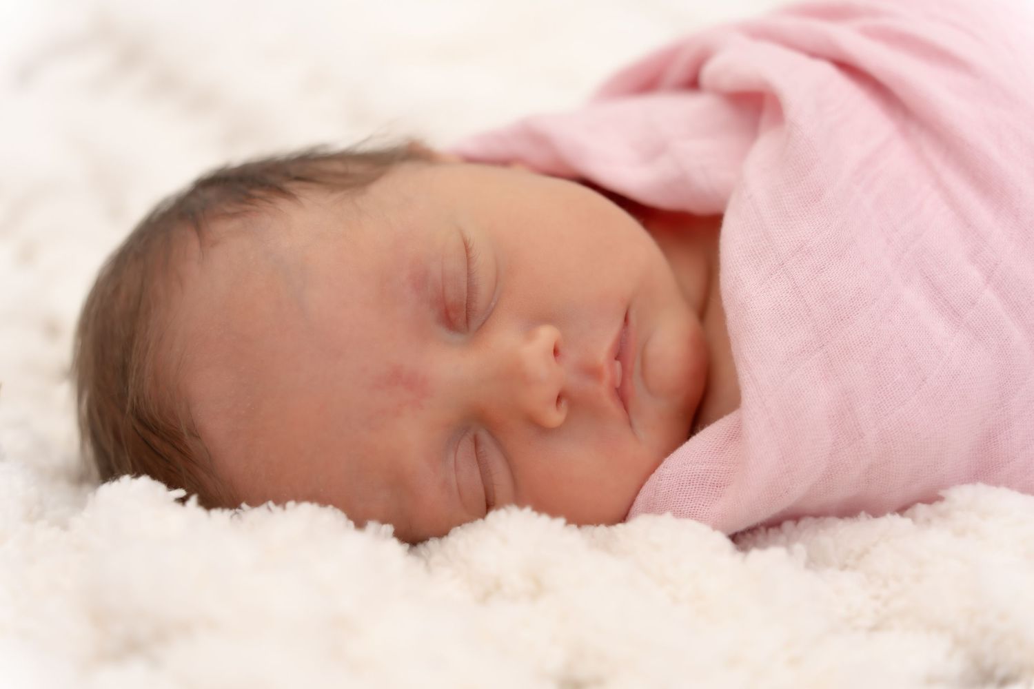 Newborn baby sleeping peacefully in pink blankets with soft lighting.