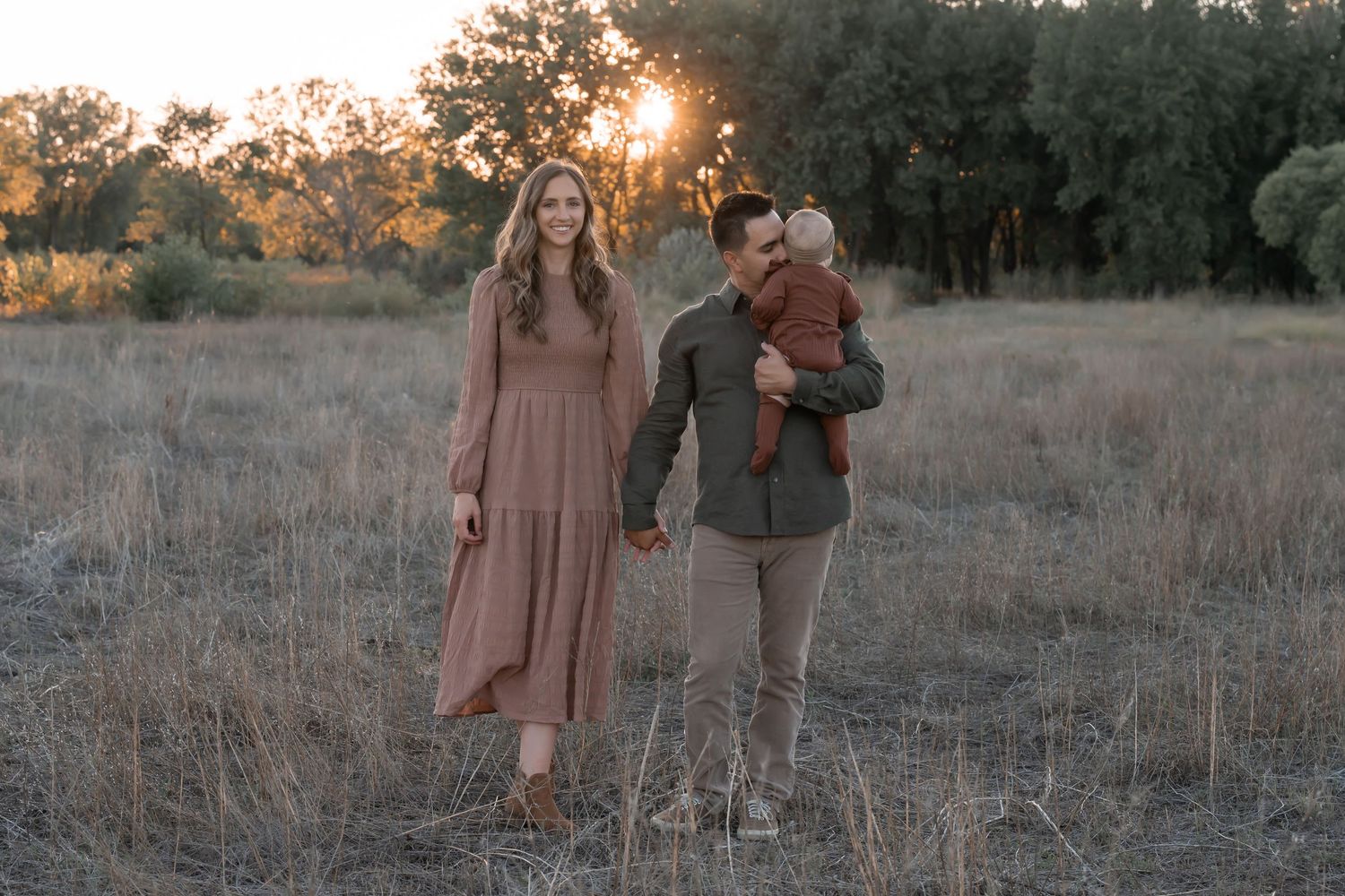 Couple holding hands during sunset photoshoot in rustic field setting.