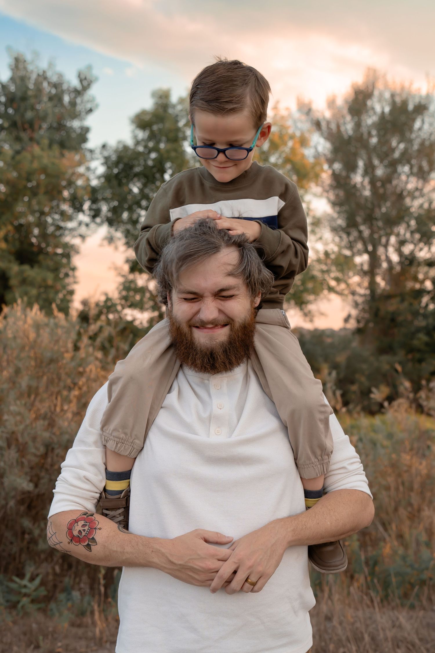 A heartwarming outdoor portrait of a child riding on shoulders against a sunset backdrop.