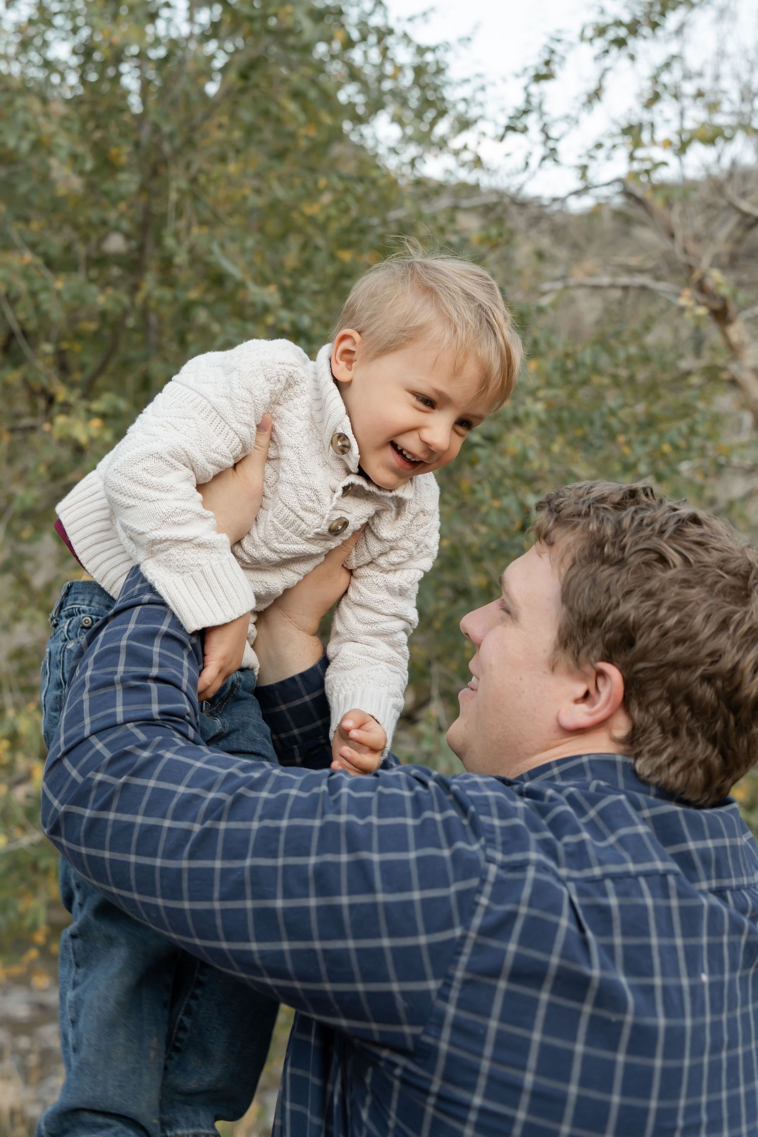 A series of candid moments showing a parent lifting and playing with a small child wearing a cream sweater outdoors.