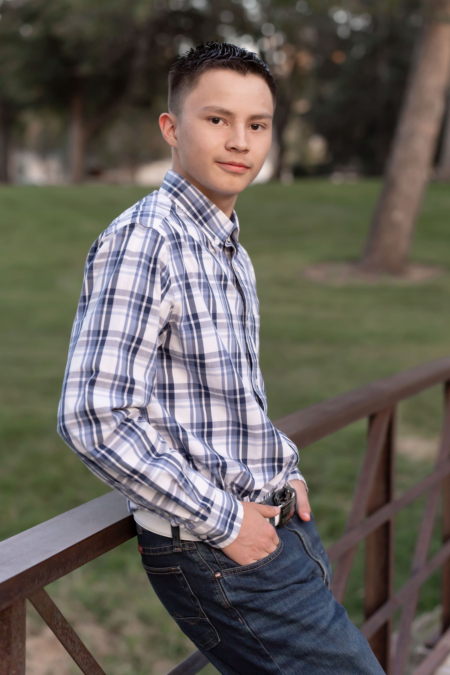 A casual portrait in a plaid button-down shirt sitting on a wooden railing.