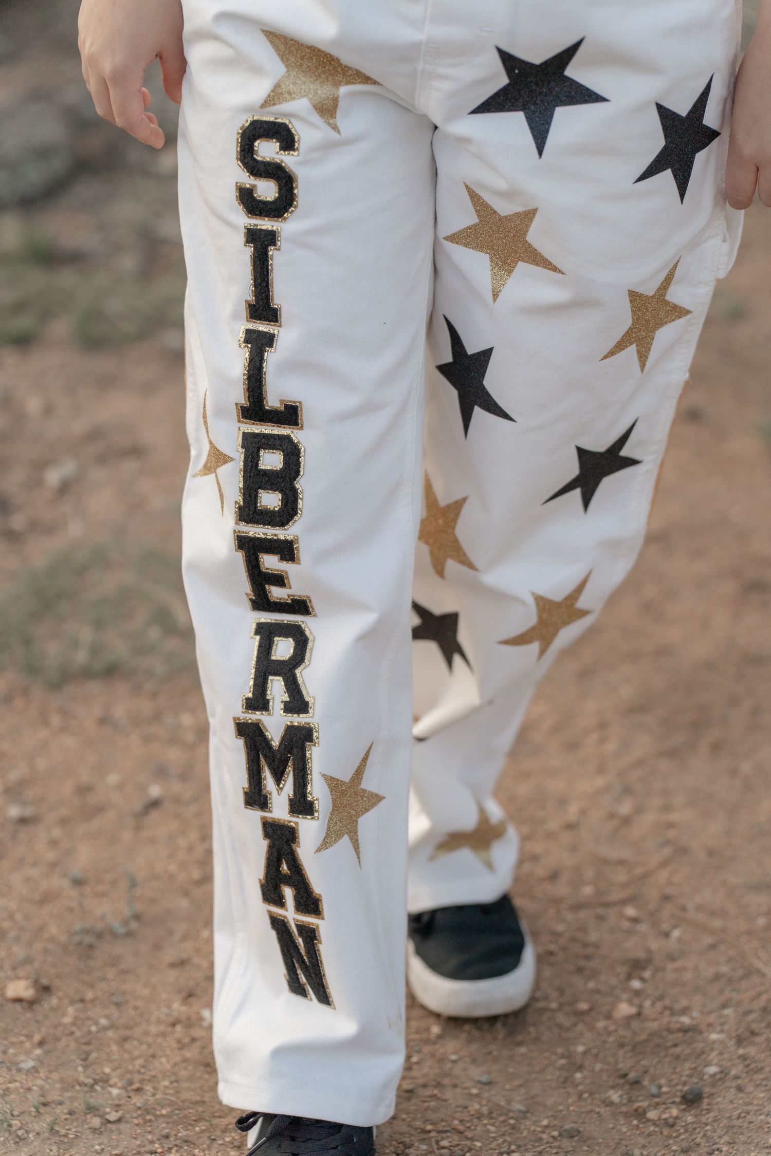 White pants with decorative gold and black star patterns and text down the leg.
