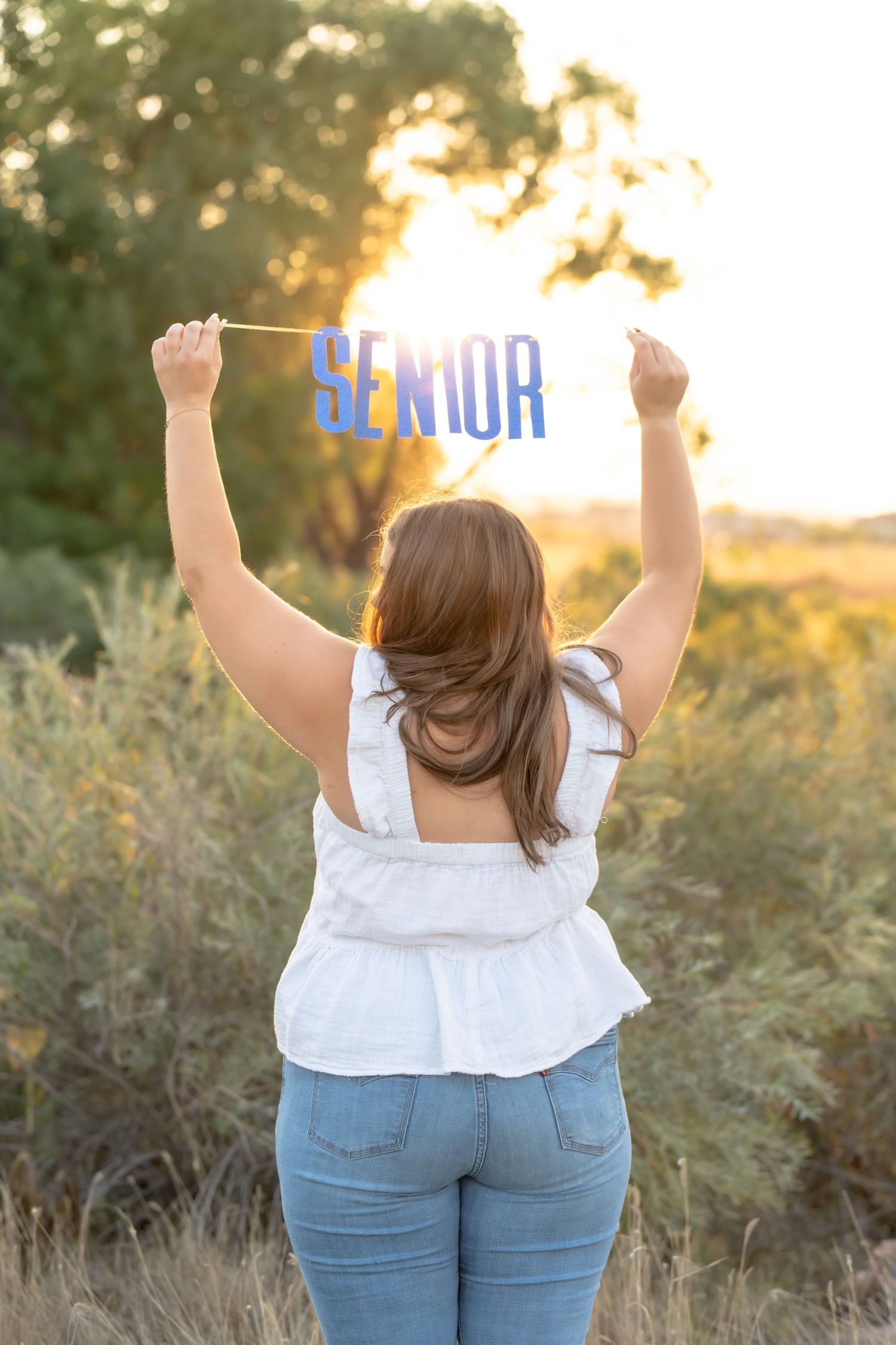 Back view of someone in white shirt and jeans raising their arms triumphantly at sunset.