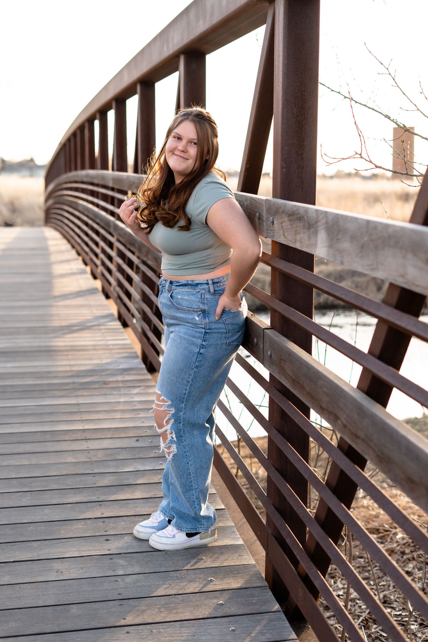Person in casual wear poses on a wooden bridge during a sunny outdoor photoshoot.