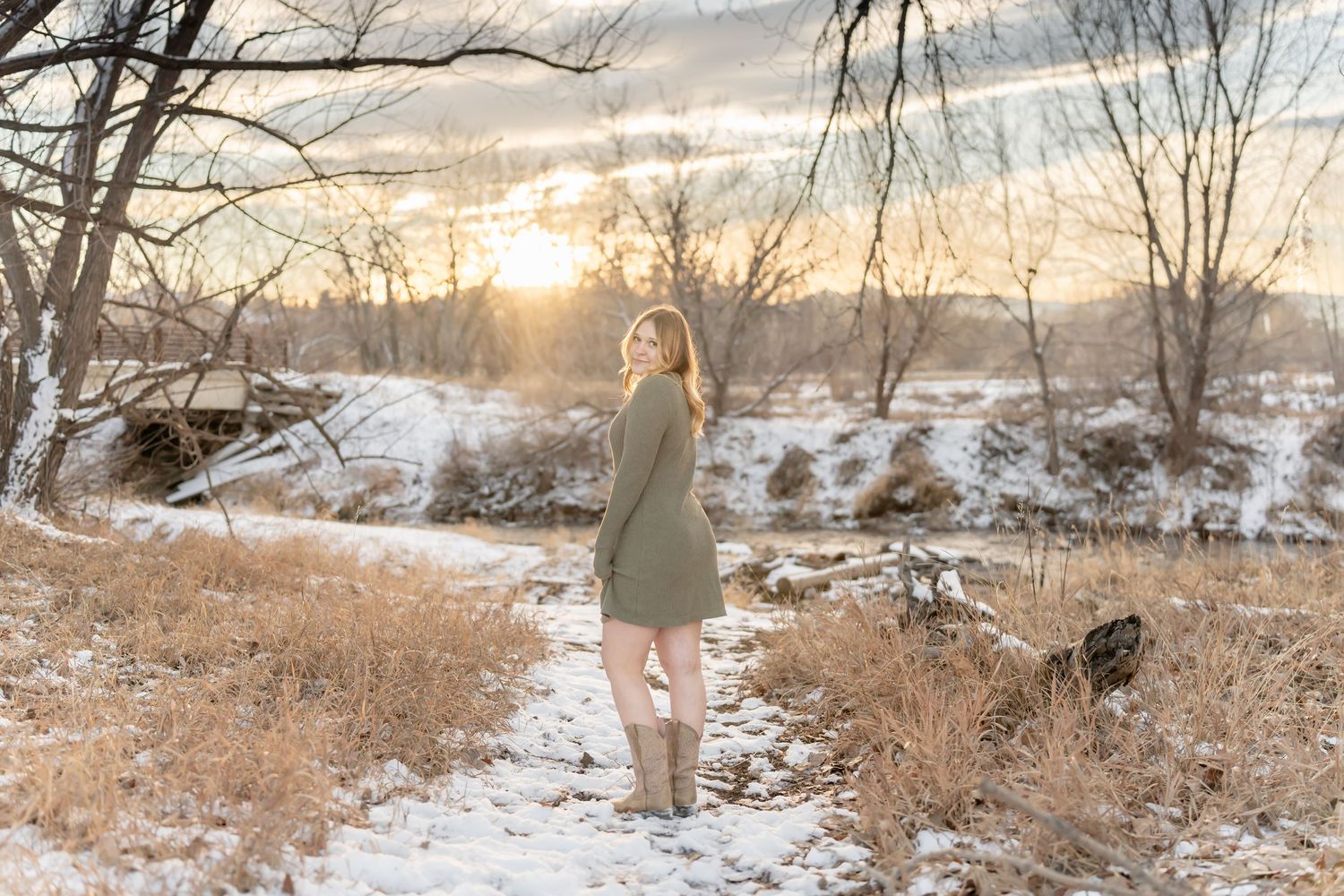Person in green dress poses in snowy winter landscape during golden hour.