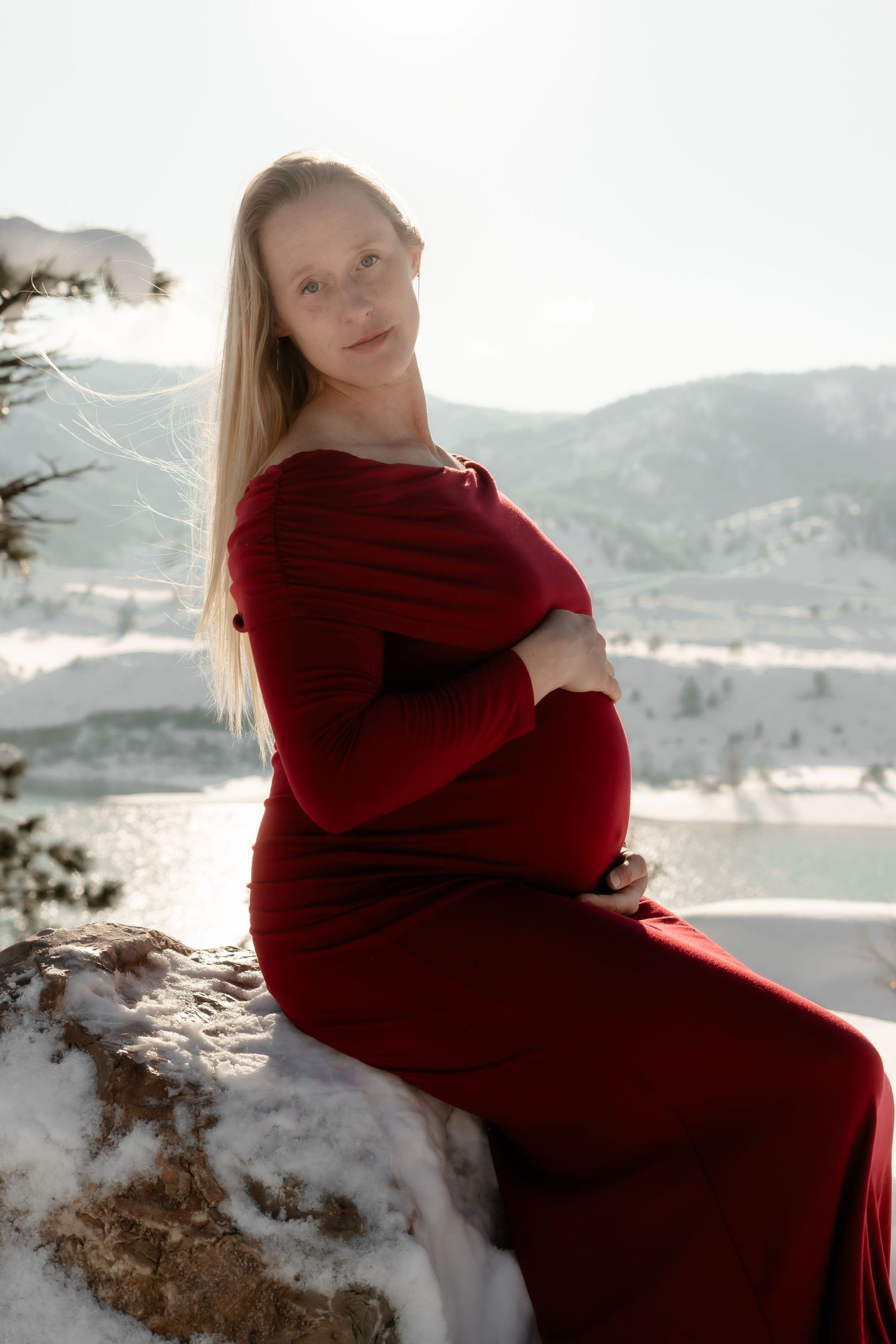 Winter maternity portrait with mountain lake backdrop.