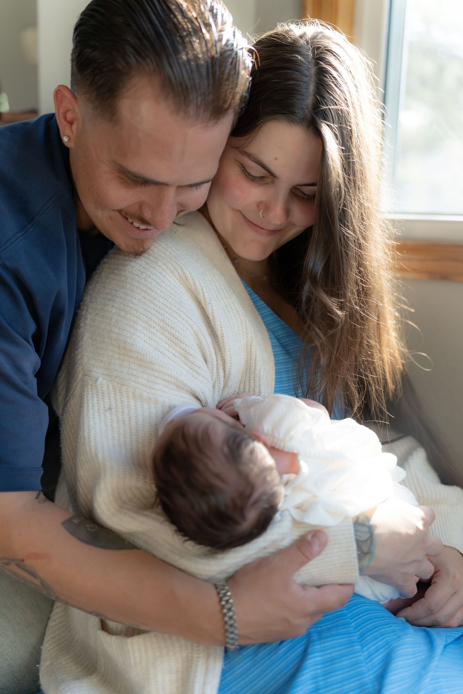 Tender moment of parents holding their newborn baby by a window.