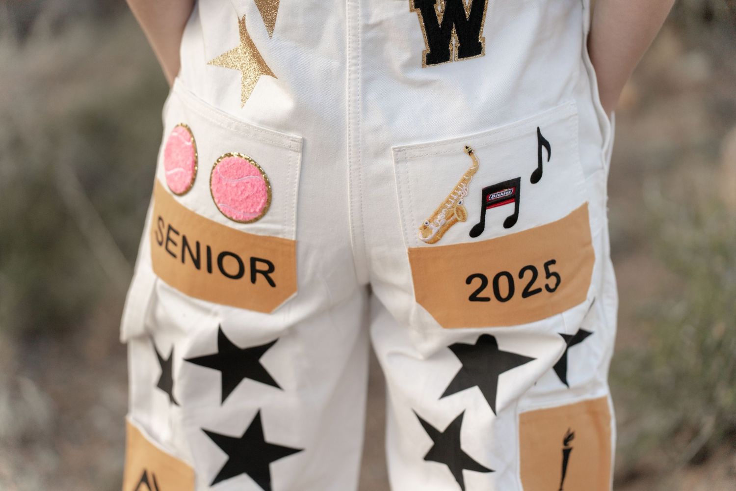 Decorated white jeans featuring black stars and graduation-themed stickers and embellishments.