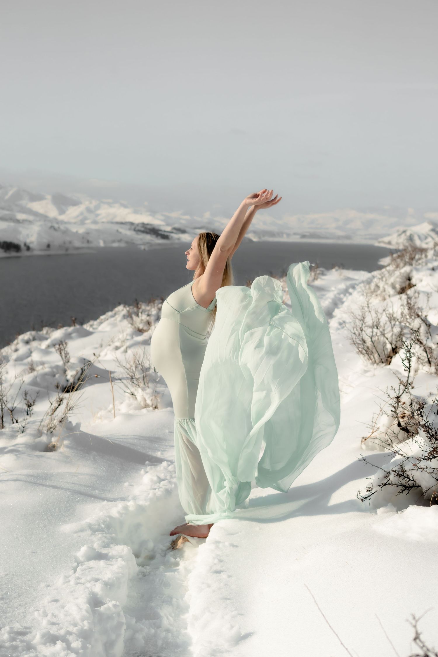 Ethereal pose in mint green dress against snowy mountain backdrop.