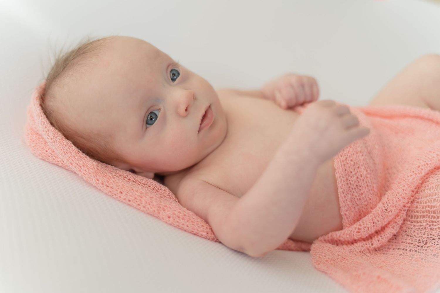 A baby lies on soft pink fabric in a gentle sleeping pose.