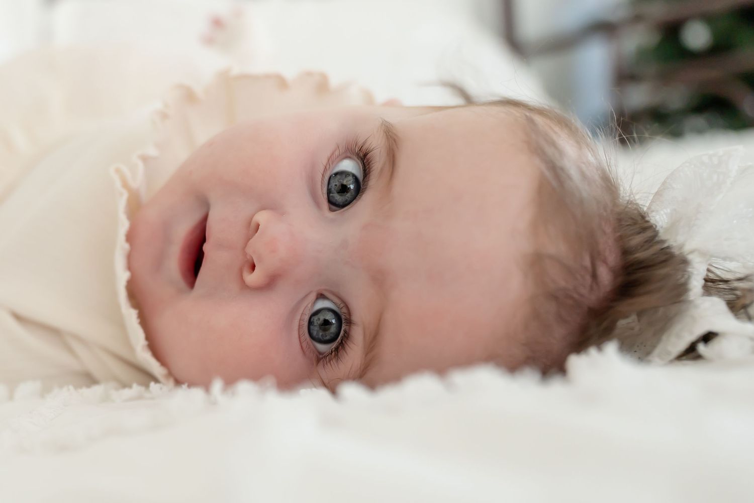 A series of close-up photos showing a baby's facial expressions while lying down on white bedding.