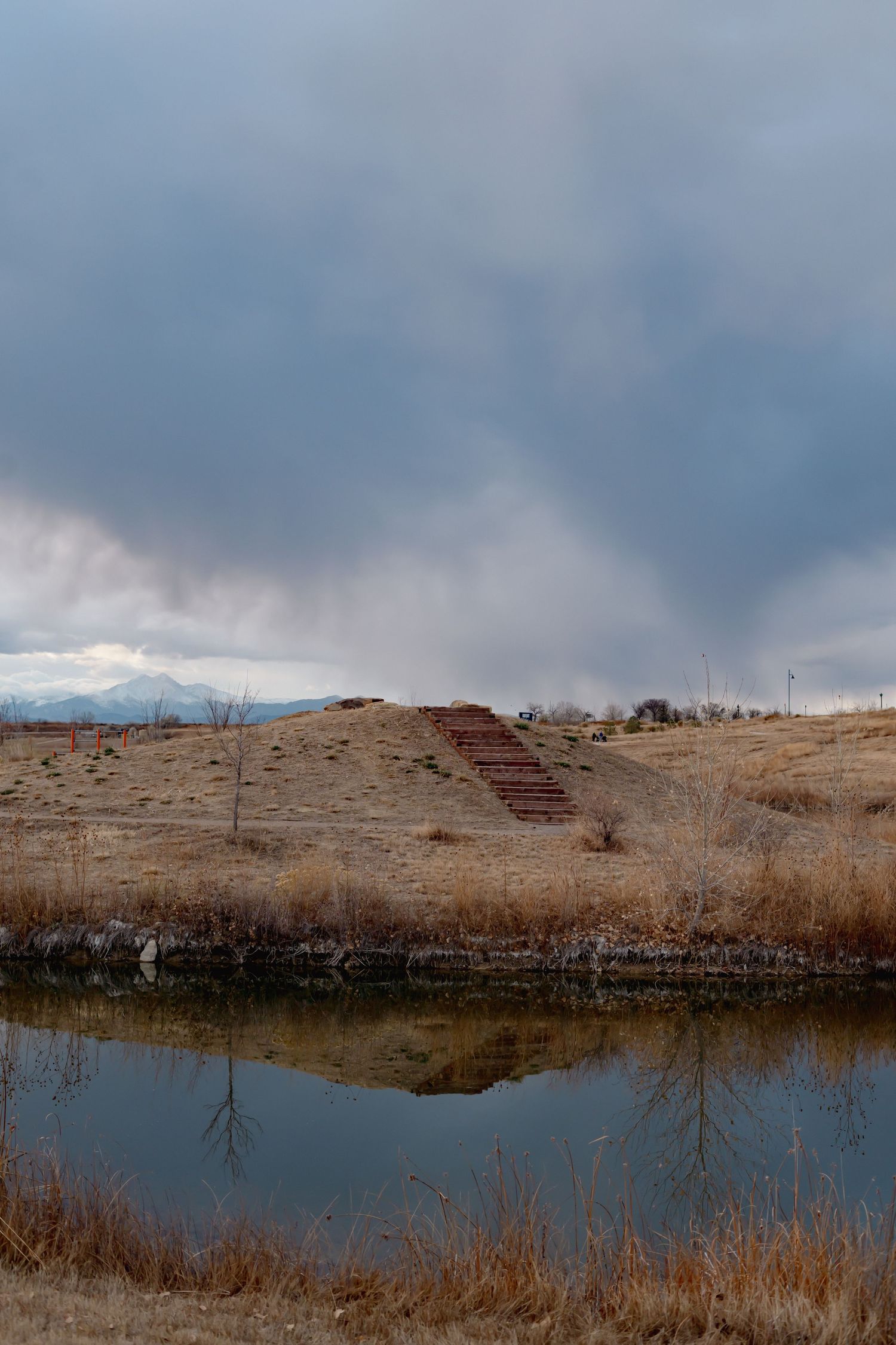 Panoramic view of a tranquil lake surrounded by brown winter grassland under cloudy skies.
