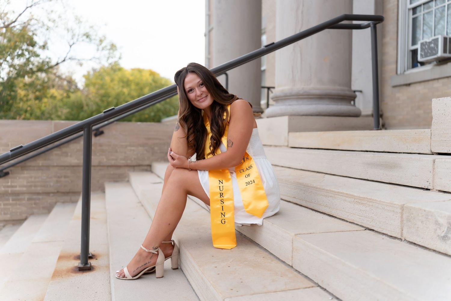 Person in yellow dress sits on concrete steps of classic building.