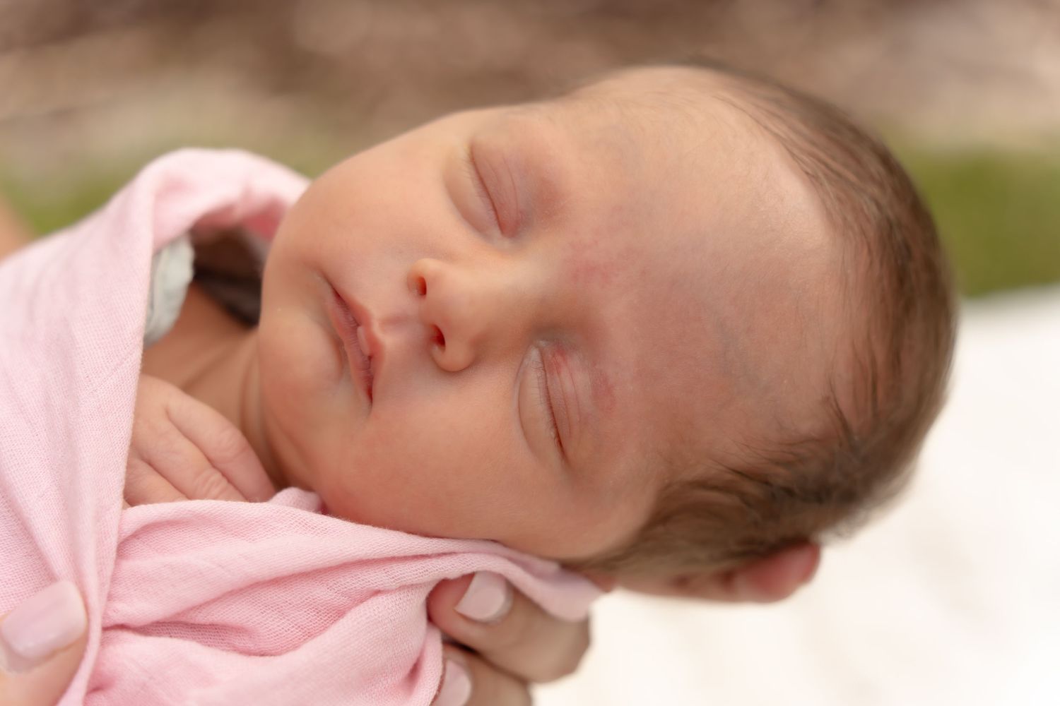 Infant resting on soft pink fabric with gentle natural lighting.