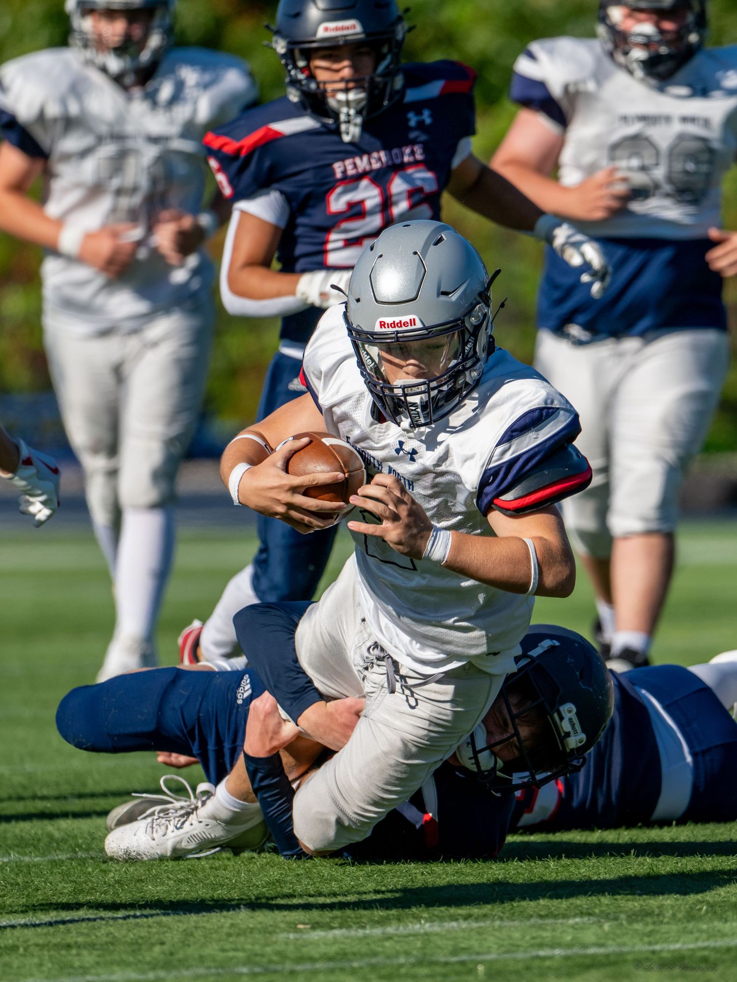 Football player carrying ball while being tackled during daytime game on grass field.