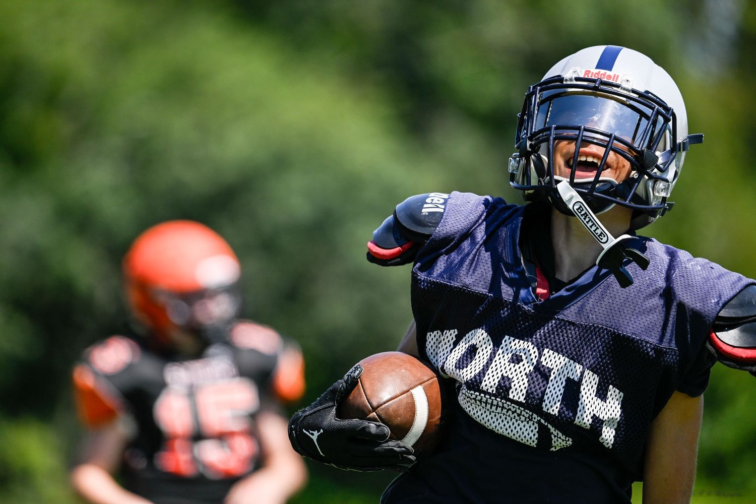 A football player in navy uniform runs with the football during a sunny game.