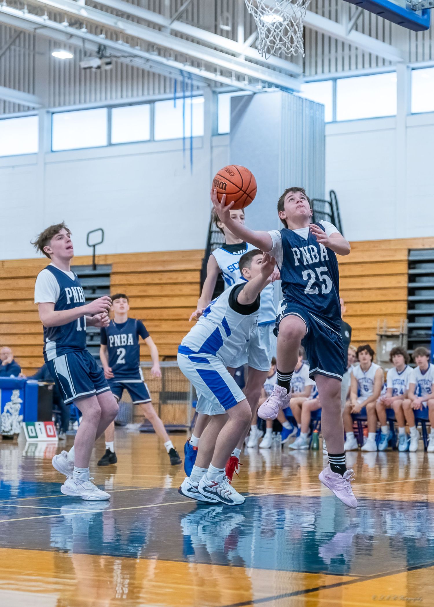 Youth basketball players in action during competitive game in school gymnasium.
