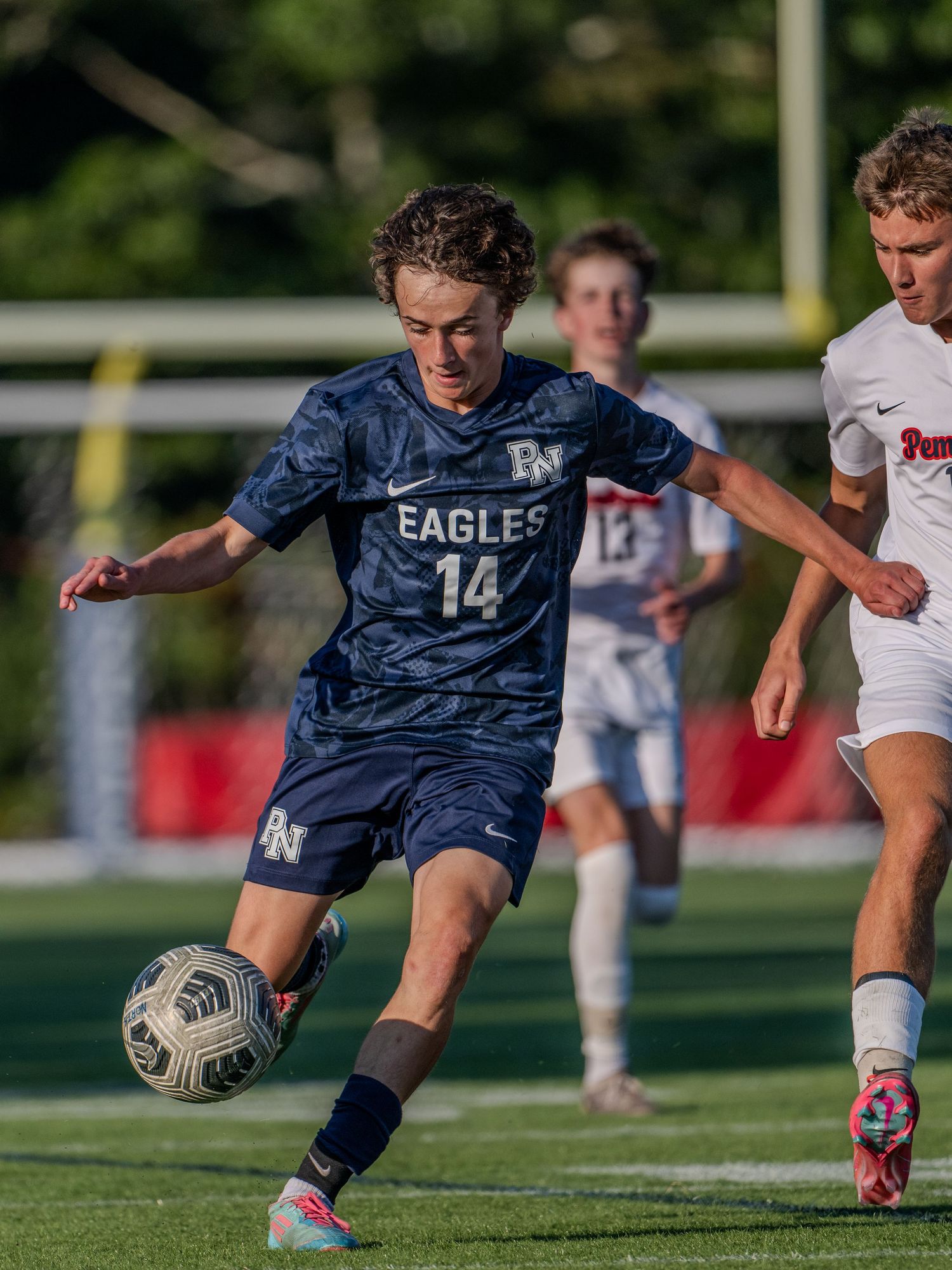 Soccer player in navy uniform dribbling ball during competitive match on grass field.