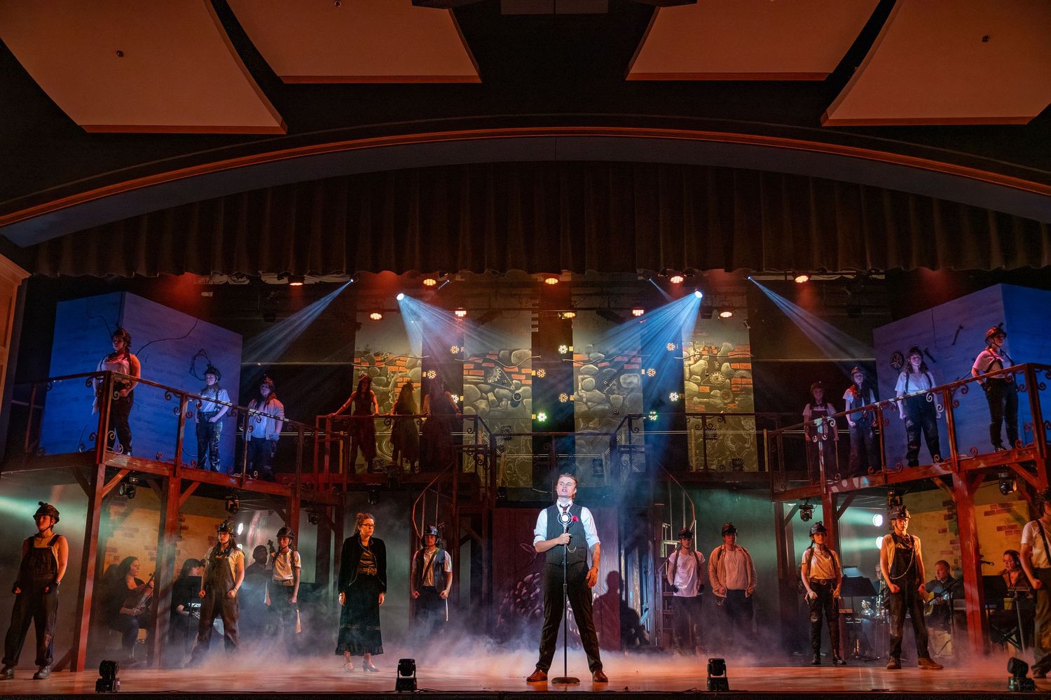 Wide shot of theatrical stage performance with dramatic lighting and fog effects.
