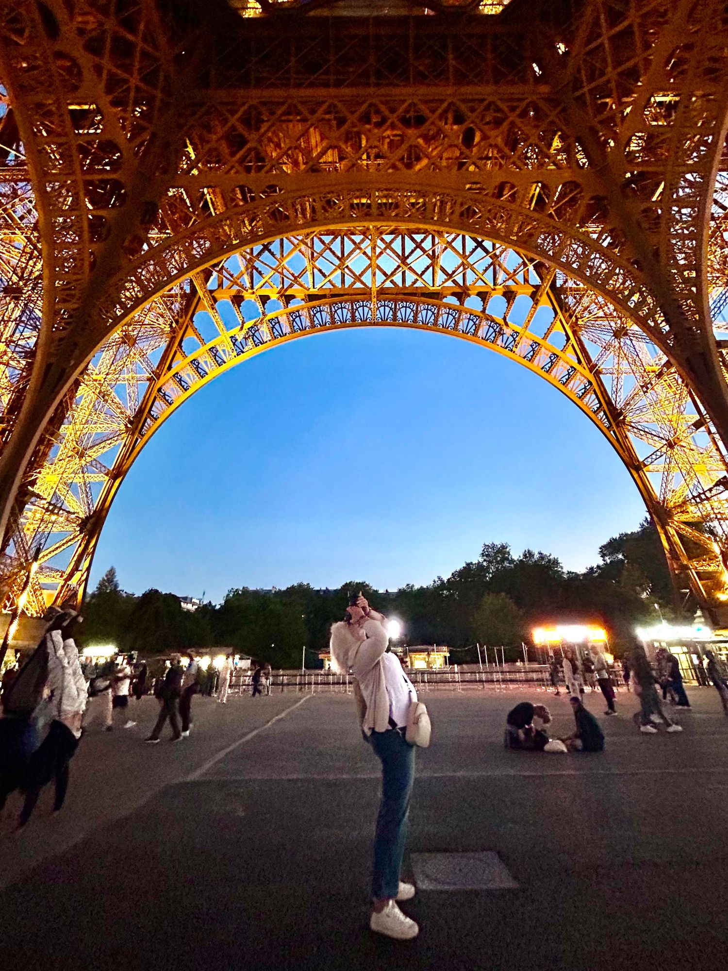 Illuminated Eiffel Tower base at dusk creating dramatic arches and silhouettes.