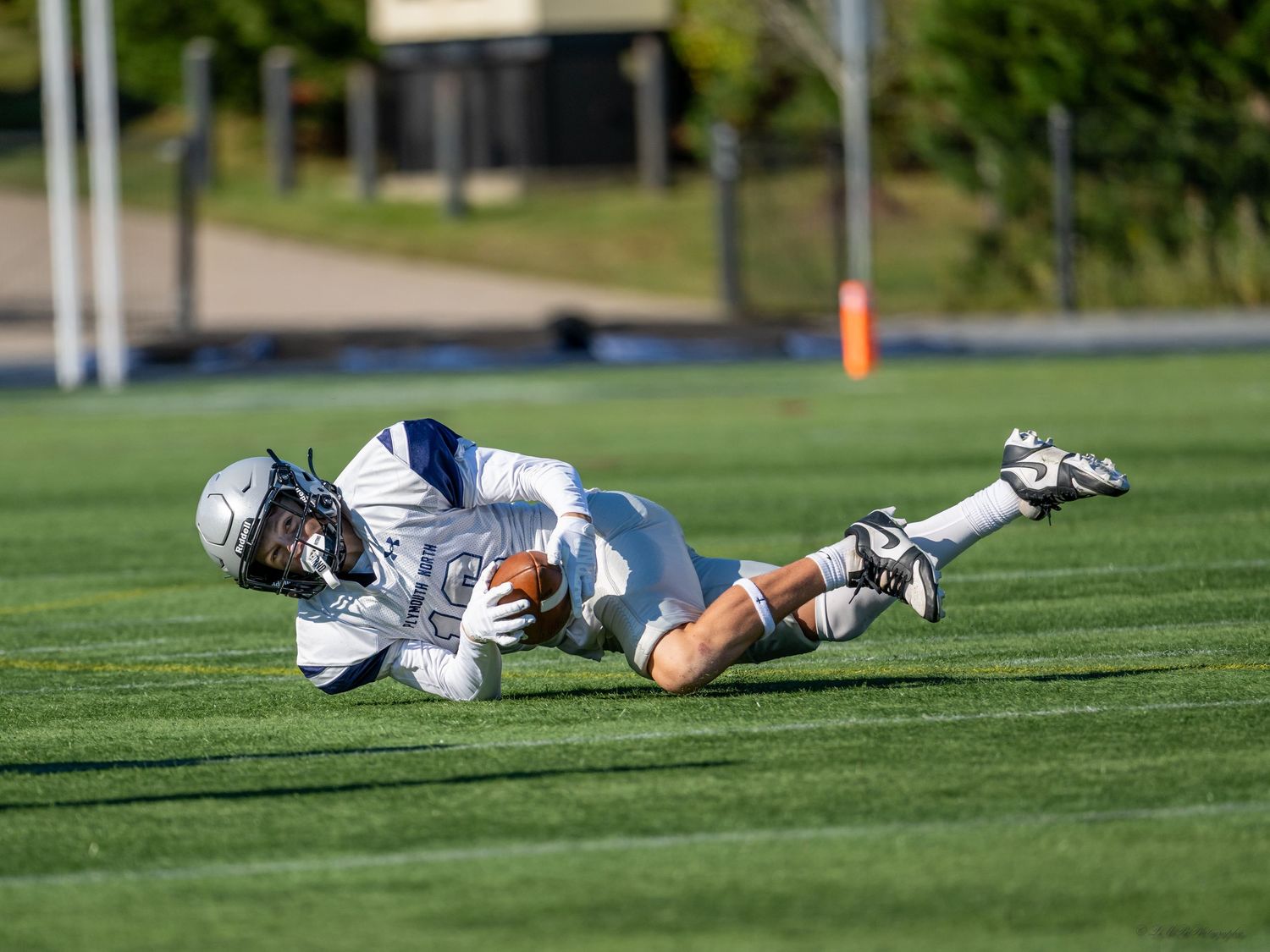 Football player diving to make a catch on green turf field during daytime game.