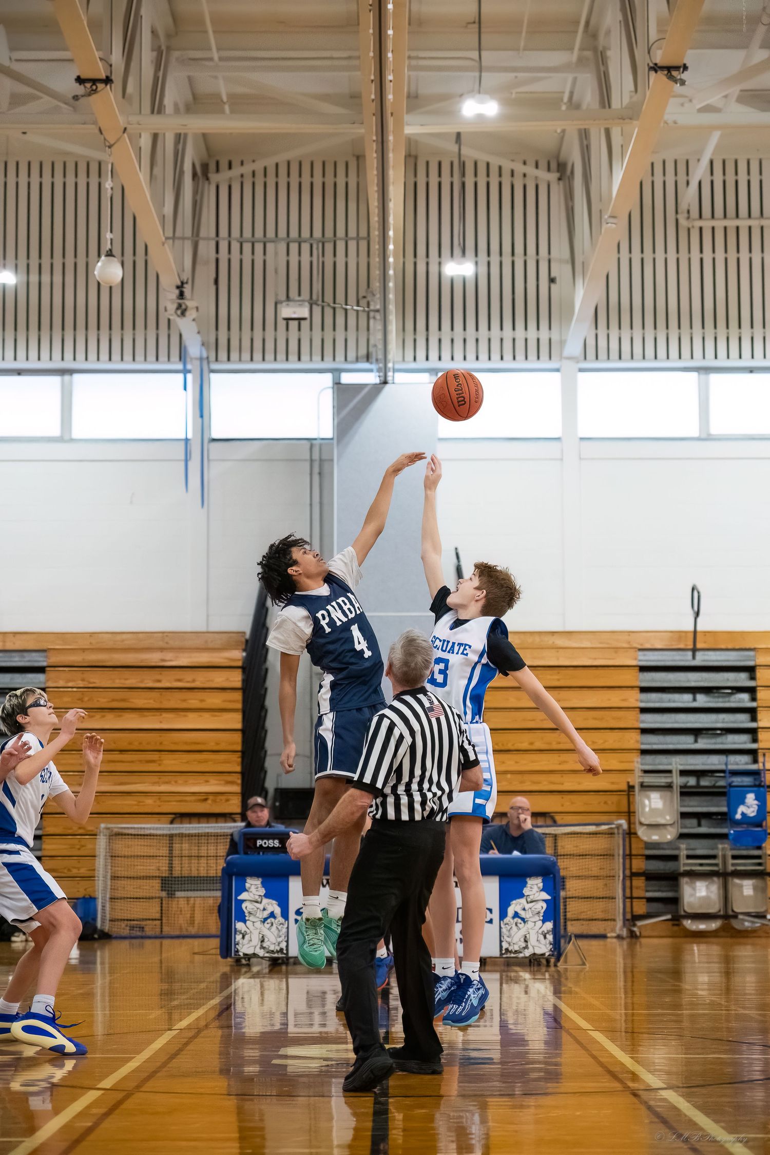 Basketball players jumping for tipoff during indoor game in school gymnasium.
