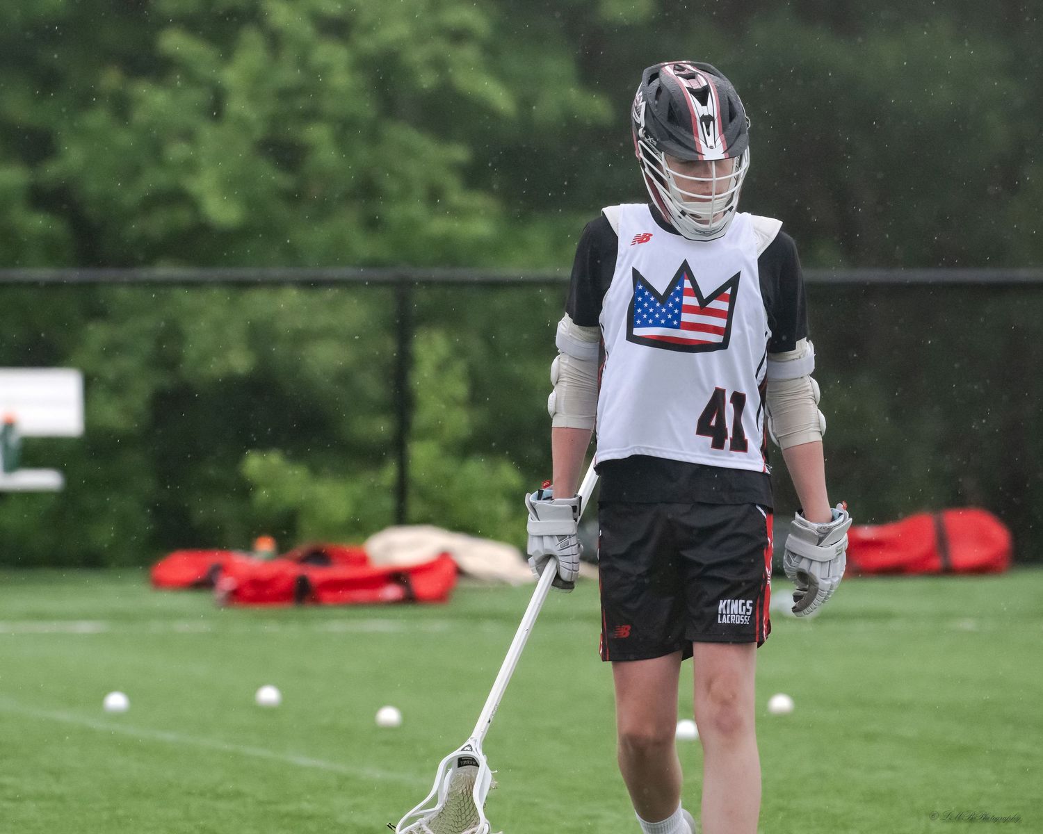 Youth lacrosse players in uniform practicing drills on grass field.