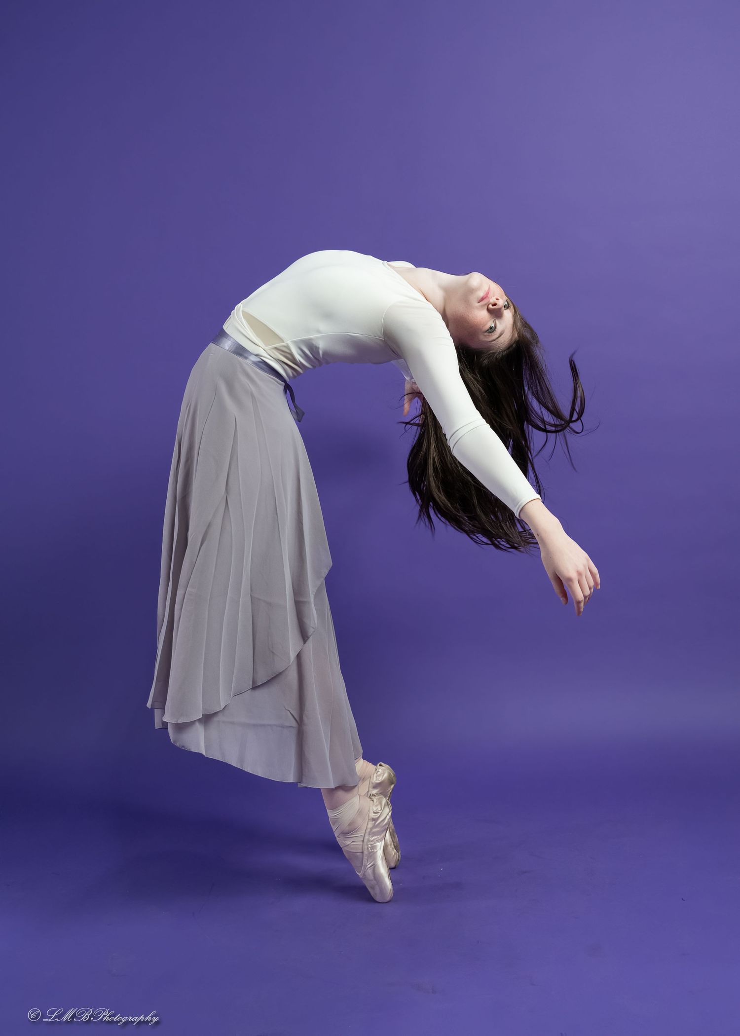 Ballet dancer in white dress performs graceful backbend sequence against purple backdrop.