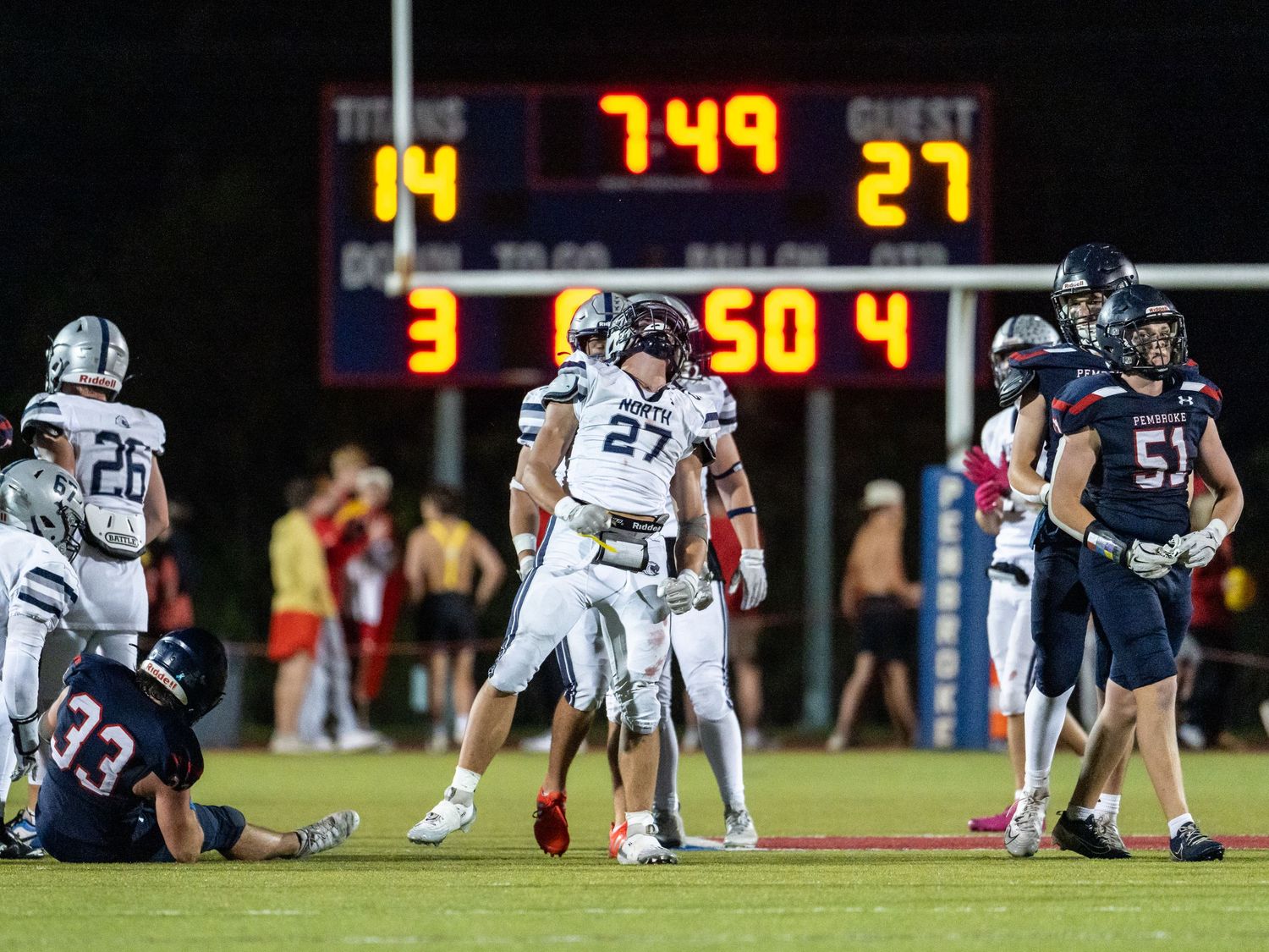 Football players on field with scoreboard showing 14-27 in background during game.