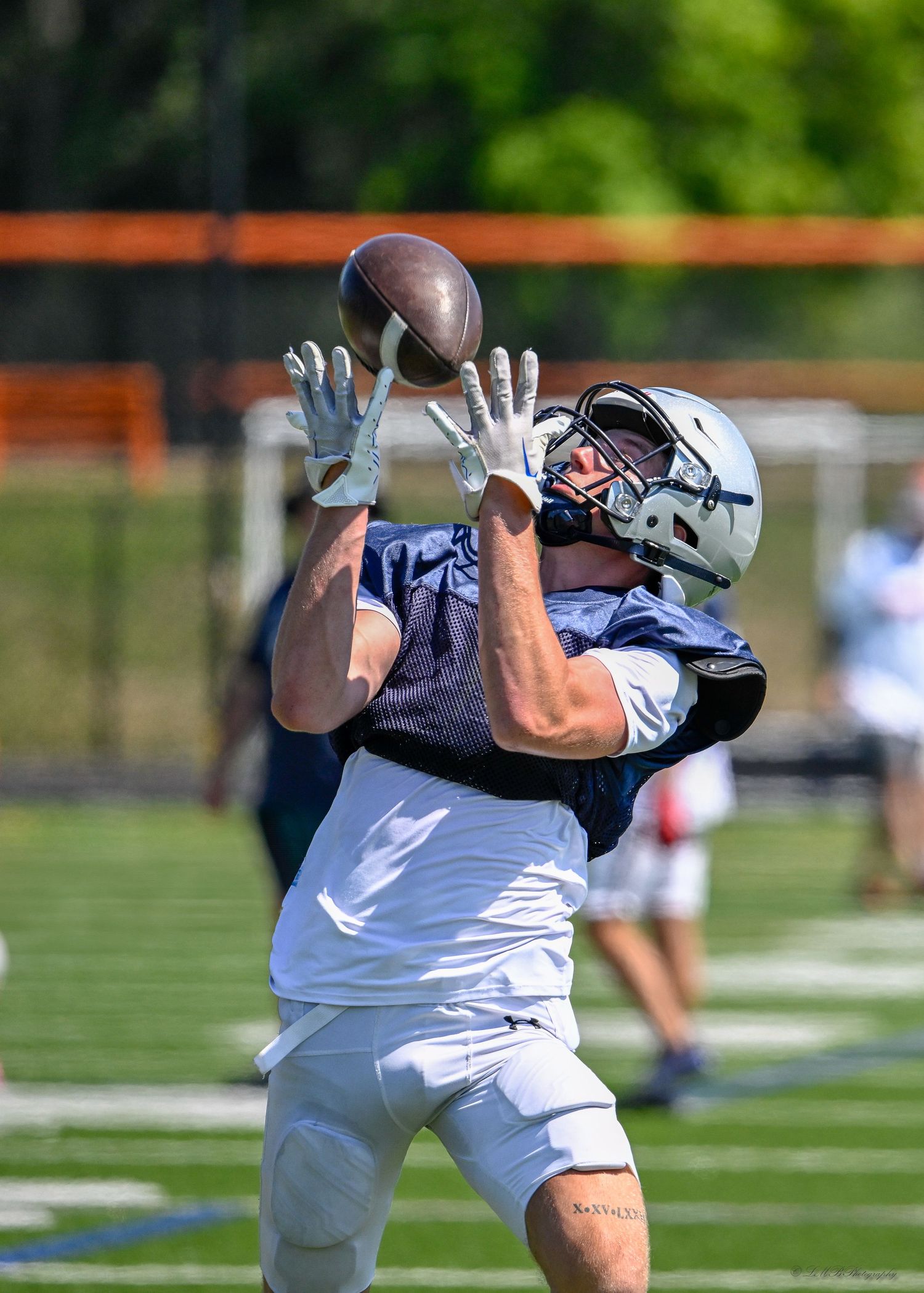 A football player reaches up to catch a pass during practice on the field.