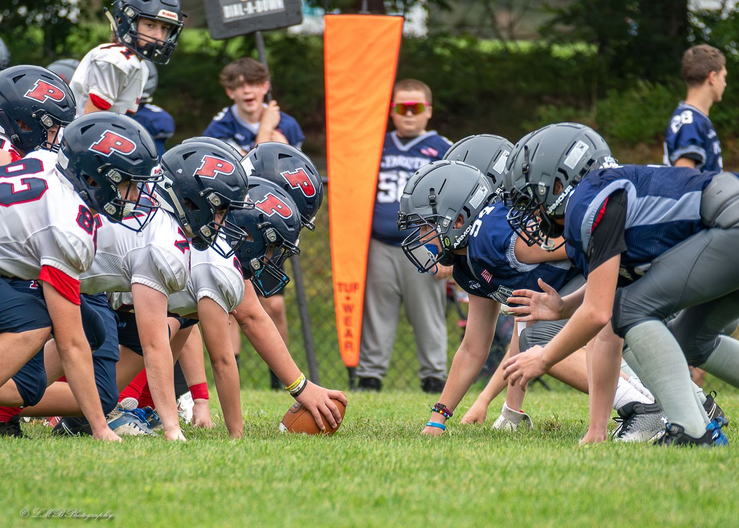 Football players lined up in formation during practice on a grass field with orange markers.