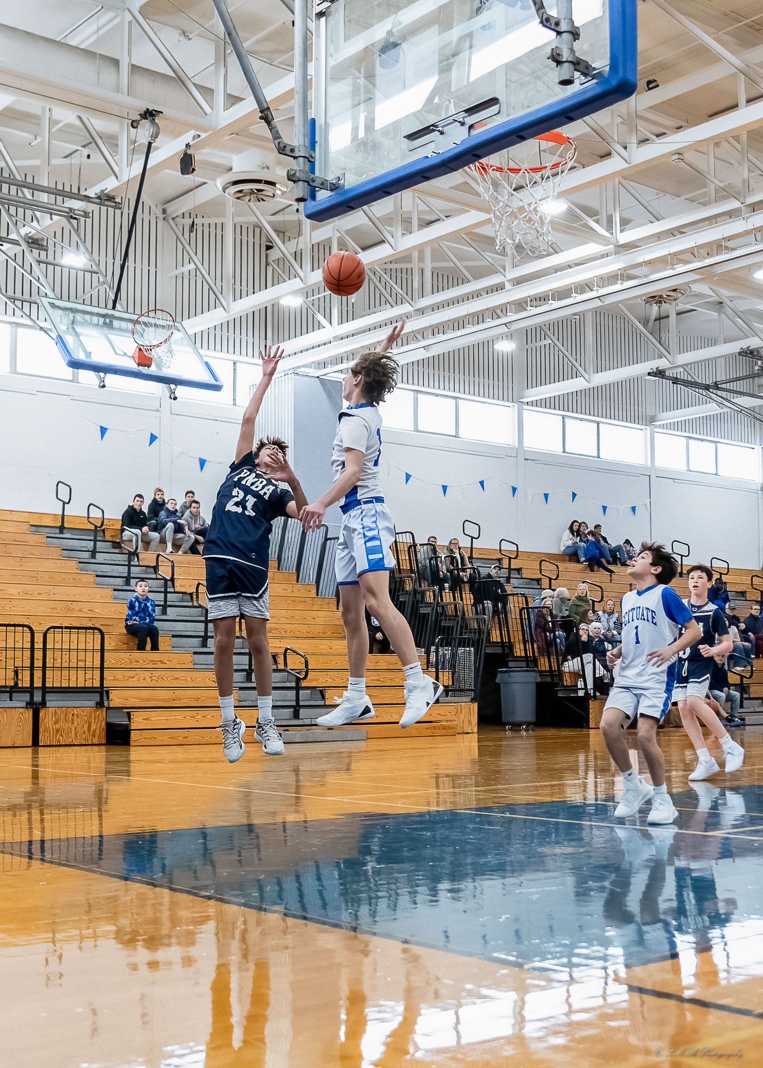 Basketball players competing for rebound during indoor game with reflective court surface.