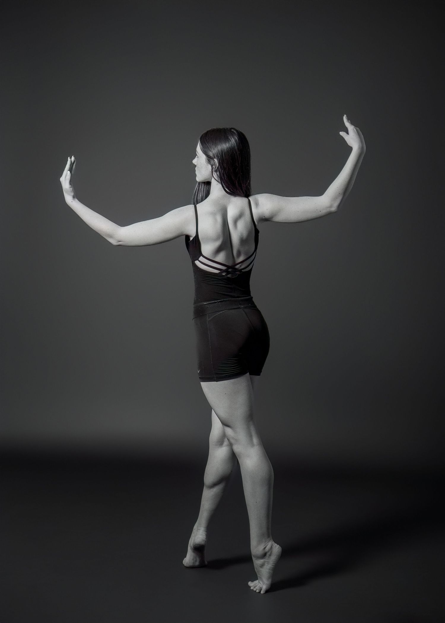 Dancer in black attire strikes graceful pose in dramatic black and white portrait.