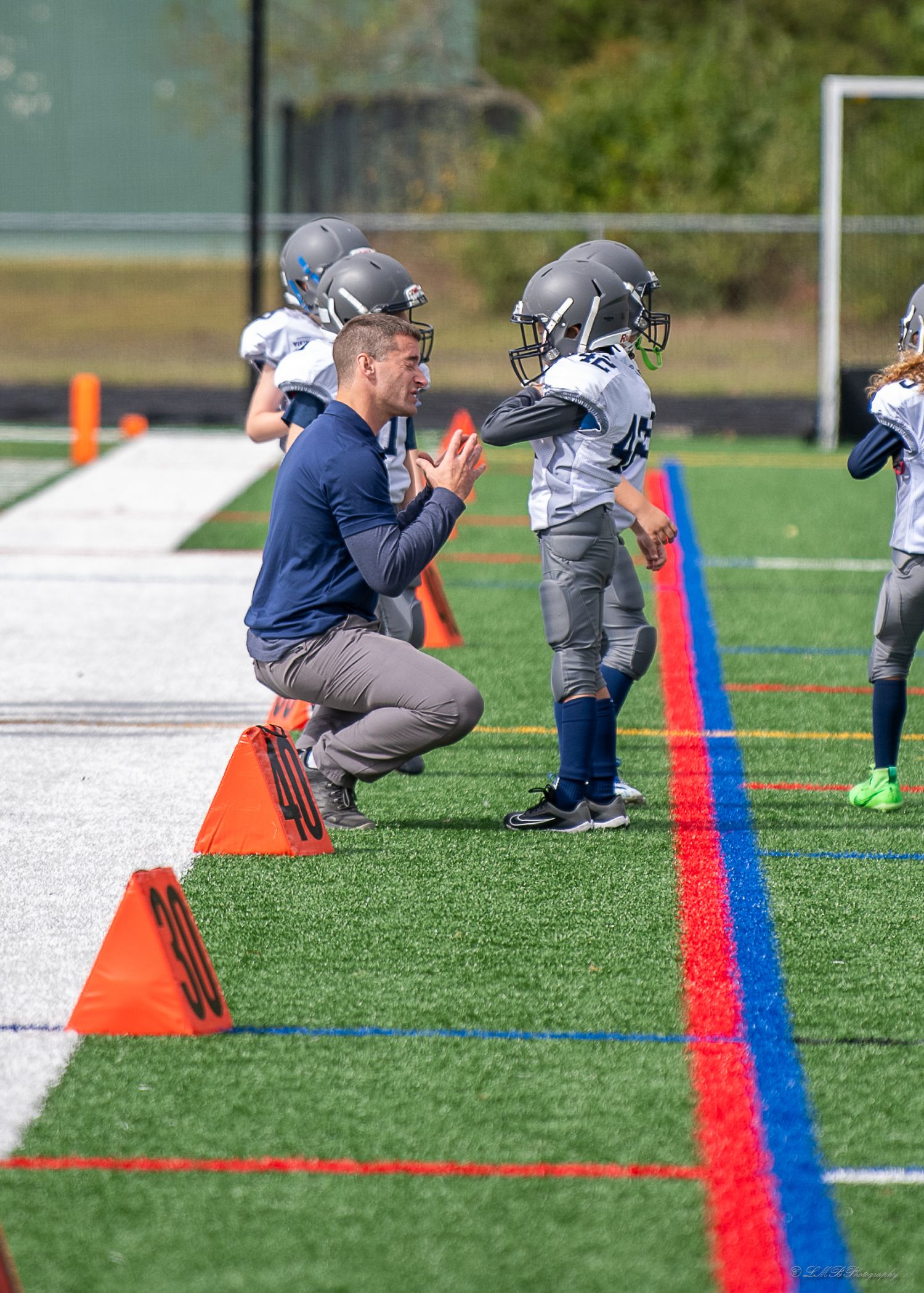 Football players practice agility drills on a green turf field with orange cones and blue lines.