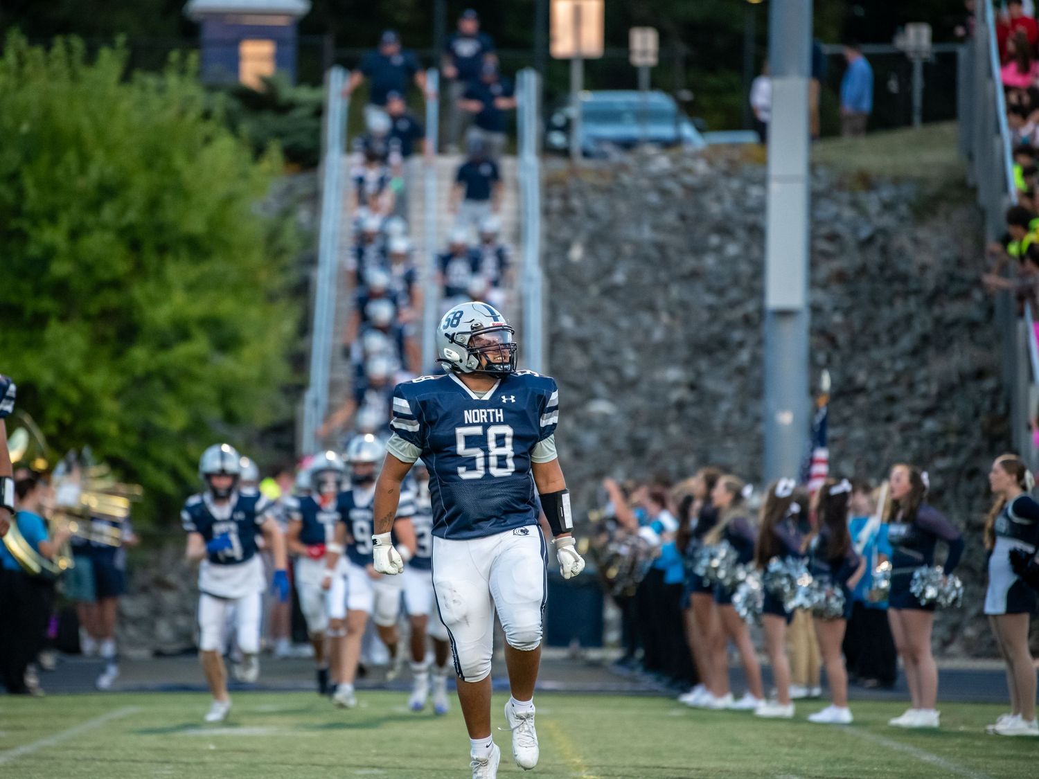 A football player in navy uniform runs onto the field past cheering fans.