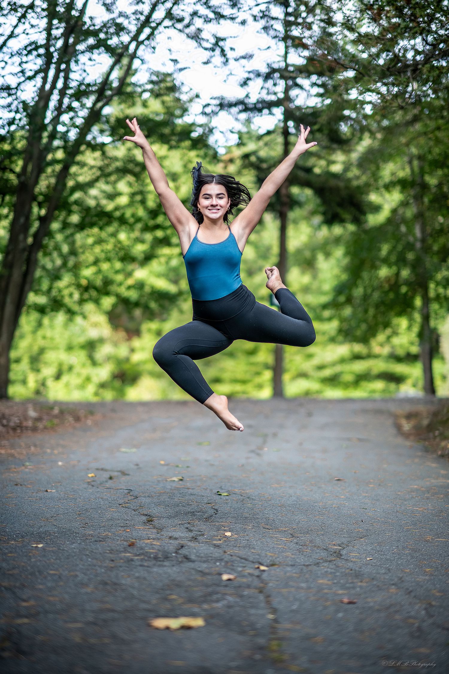 Dancer in blue leotard leaps joyfully on forest path.