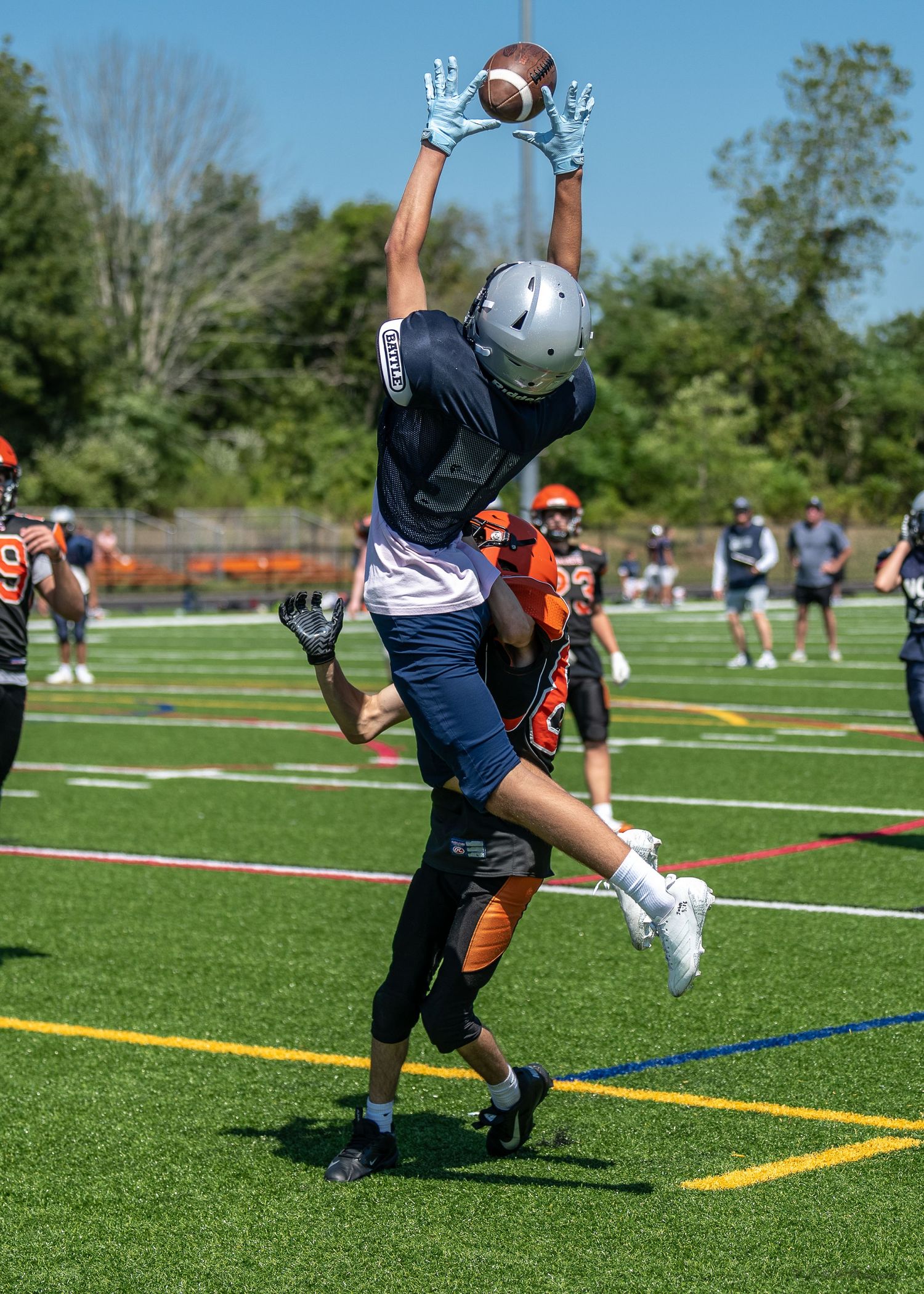 A football player leaps high to catch a pass during a game on an outdoor field.