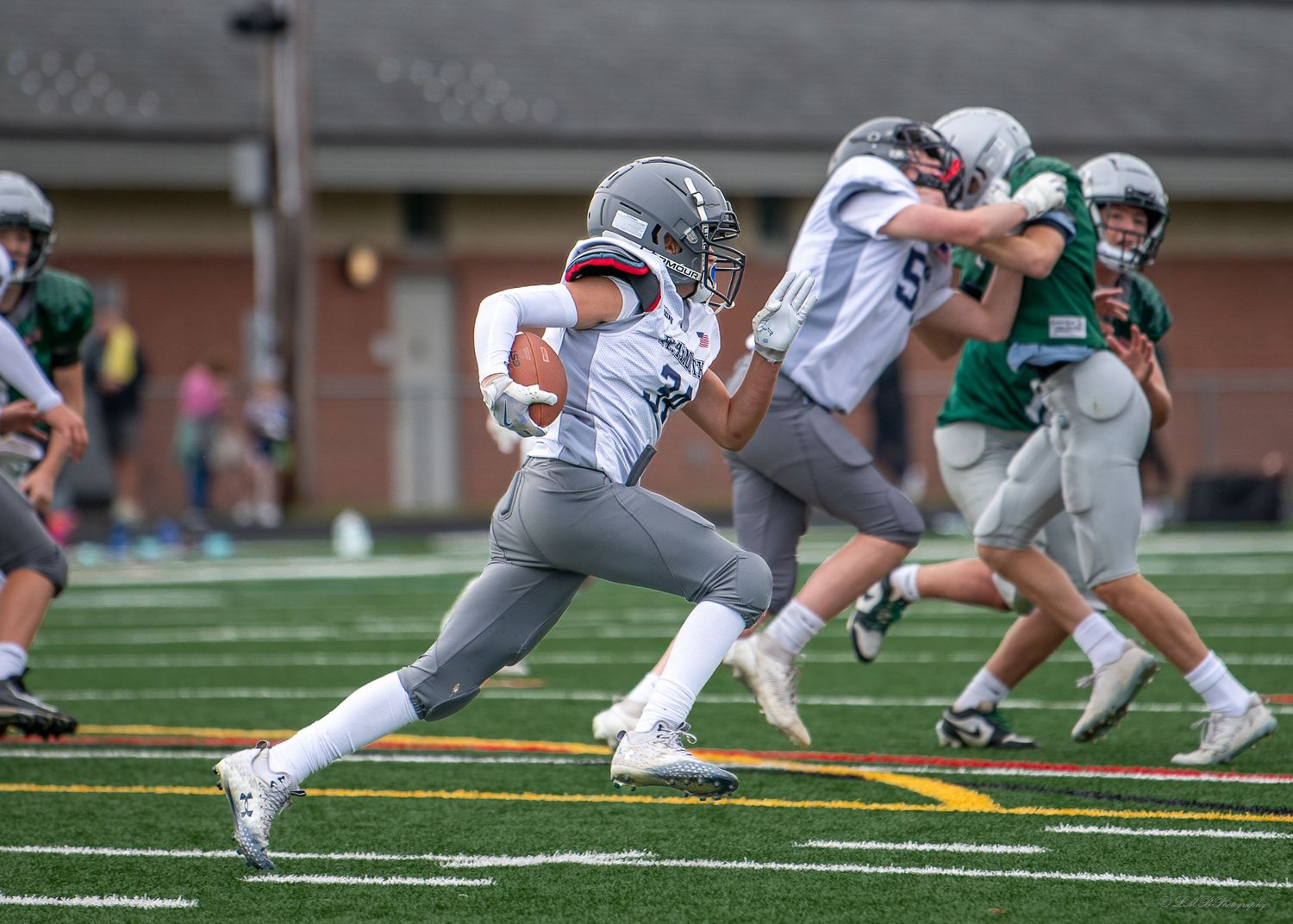 Football players in motion during offensive play on artificial turf field.