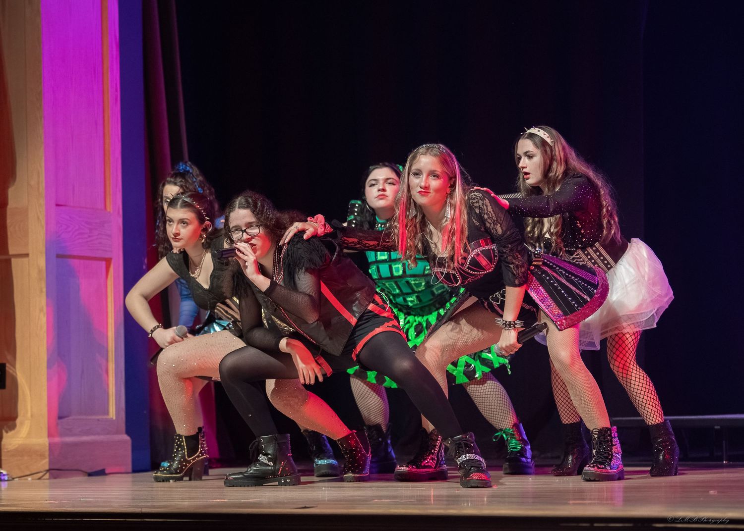 Dance ensemble performing choreographed routine on stage with dramatic purple lighting.