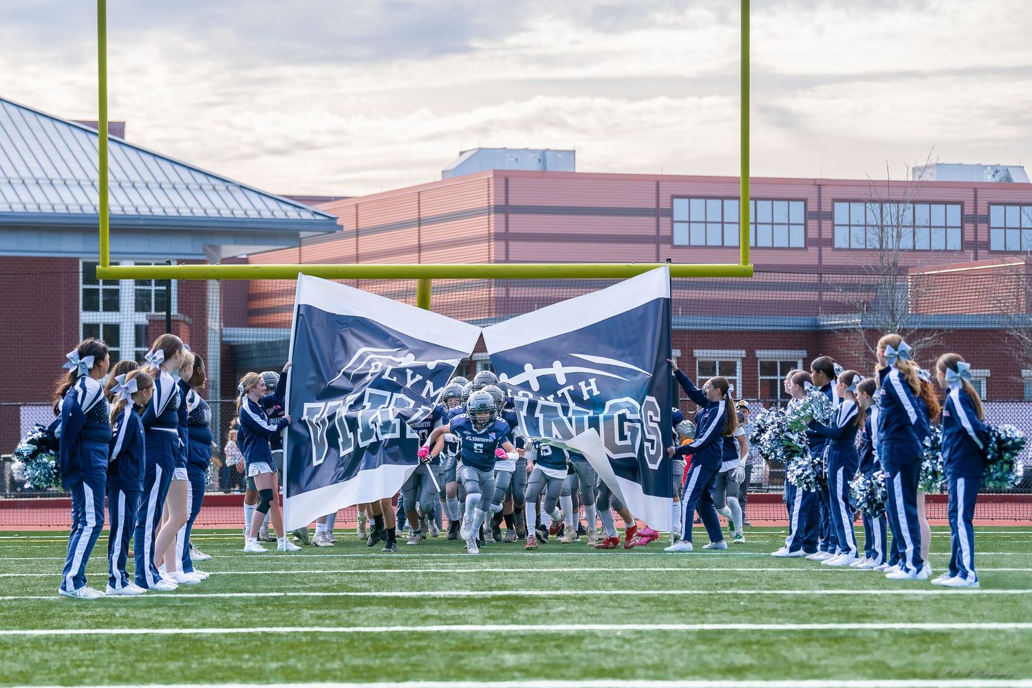 Football teams and officials gather on the field before a game at sunset.