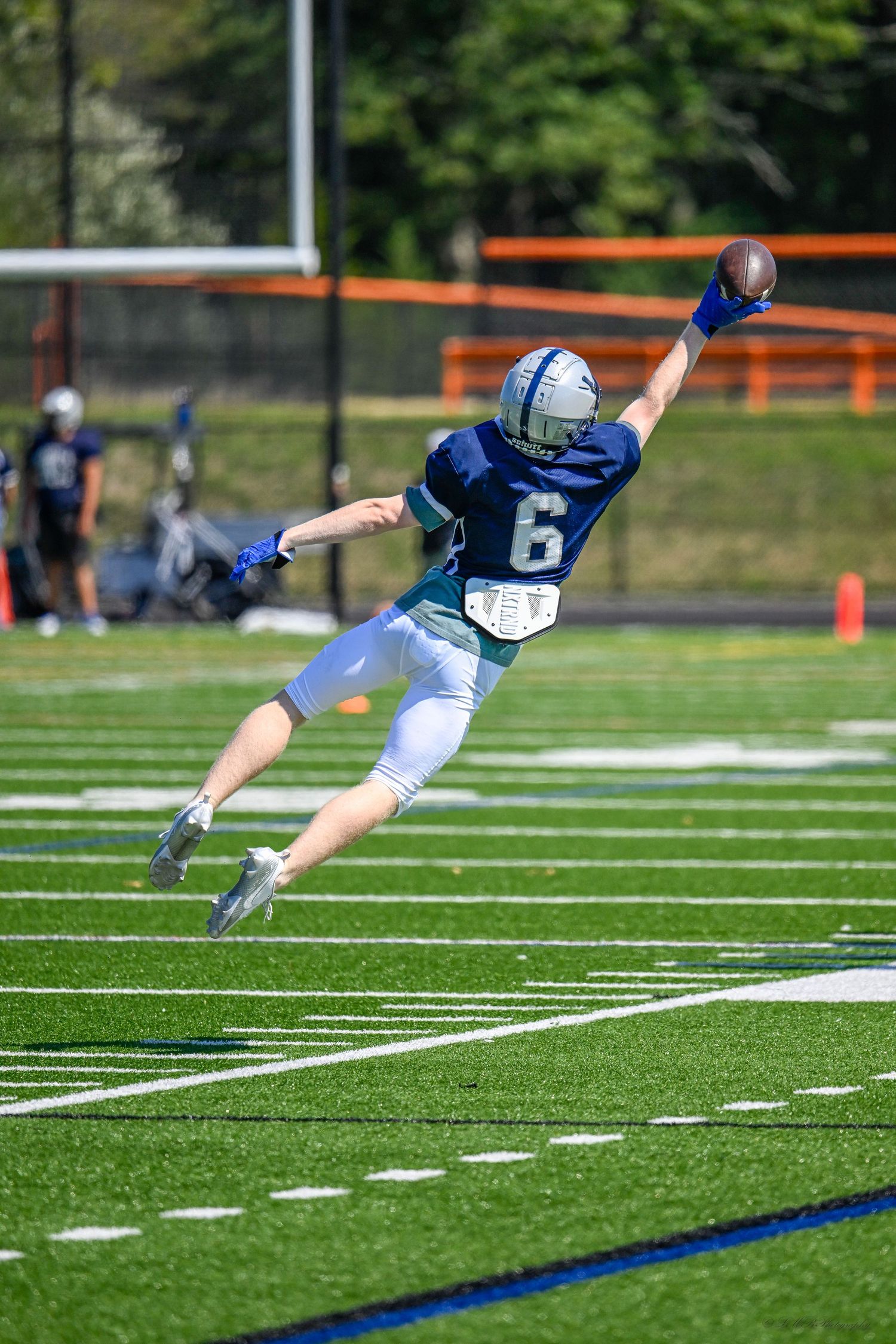 A player in blue jersey number 6 makes a diving catch attempt on the football field.