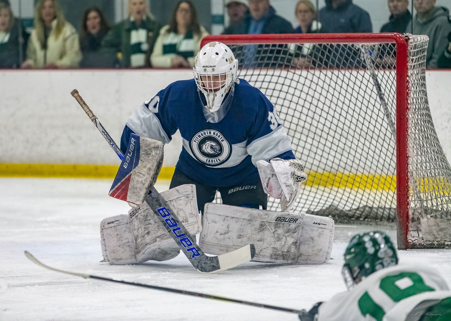 Hockey goalie in blue uniform makes a save while defending the net on ice.