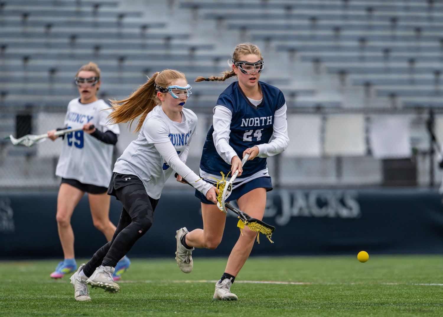 Athletes diving and reaching for balls during an intense lacrosse match on a sports field.