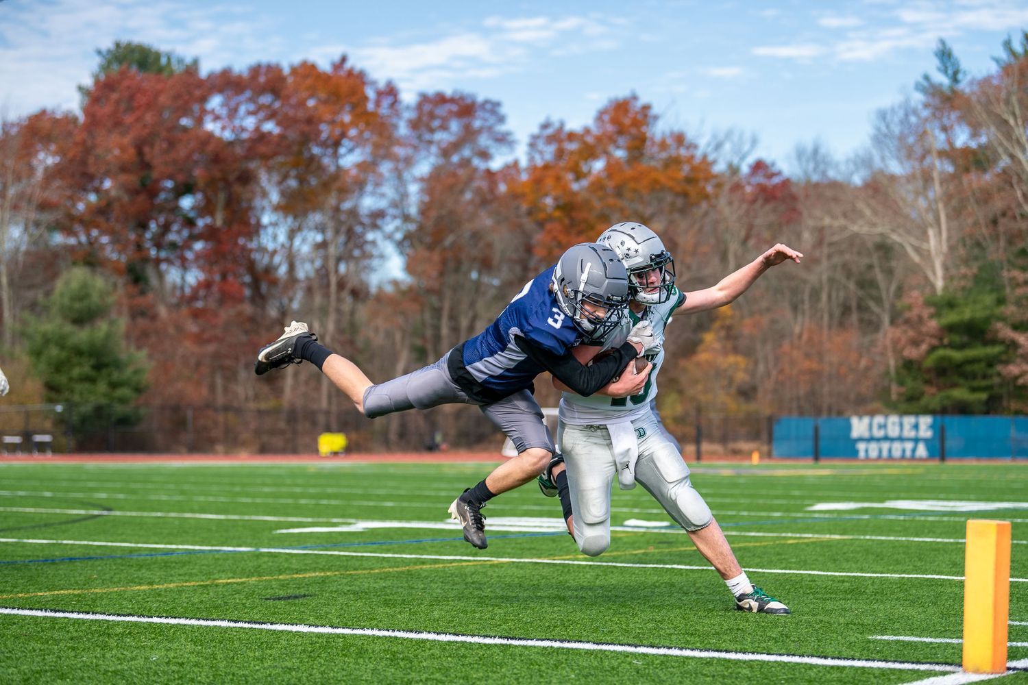 Football players diving and tackling on a grass field during an autumn game.