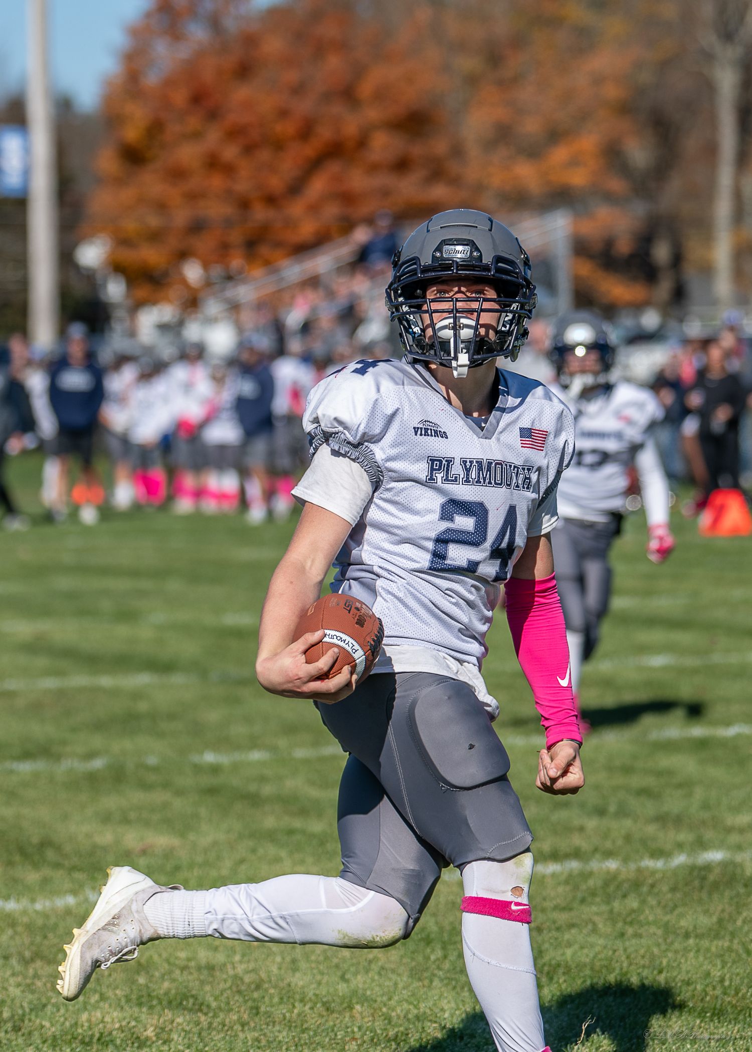 Football player in gray uniform running with ball during fall season game.