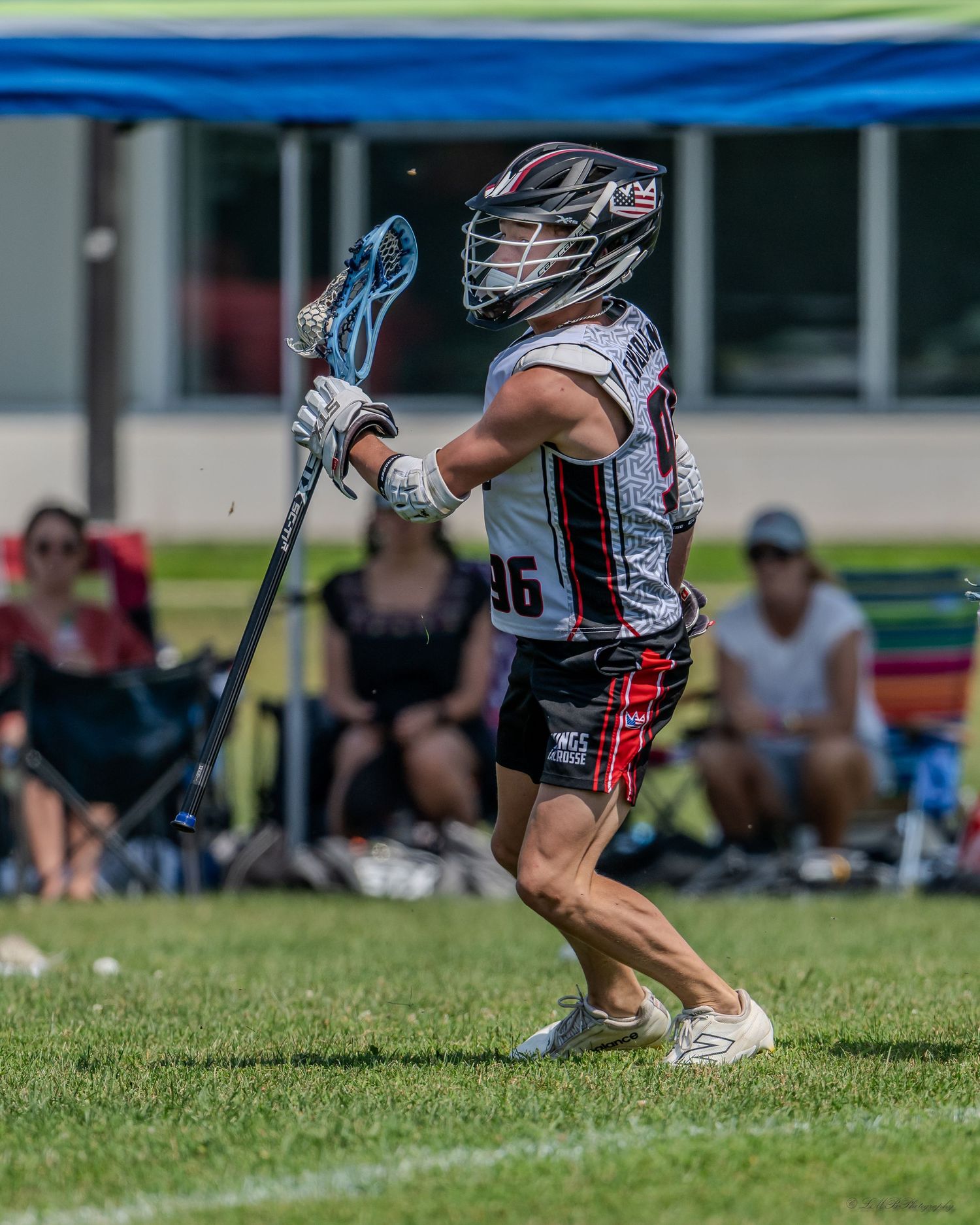 Lacrosse players in protective gear crouching low during game play on sunny field.