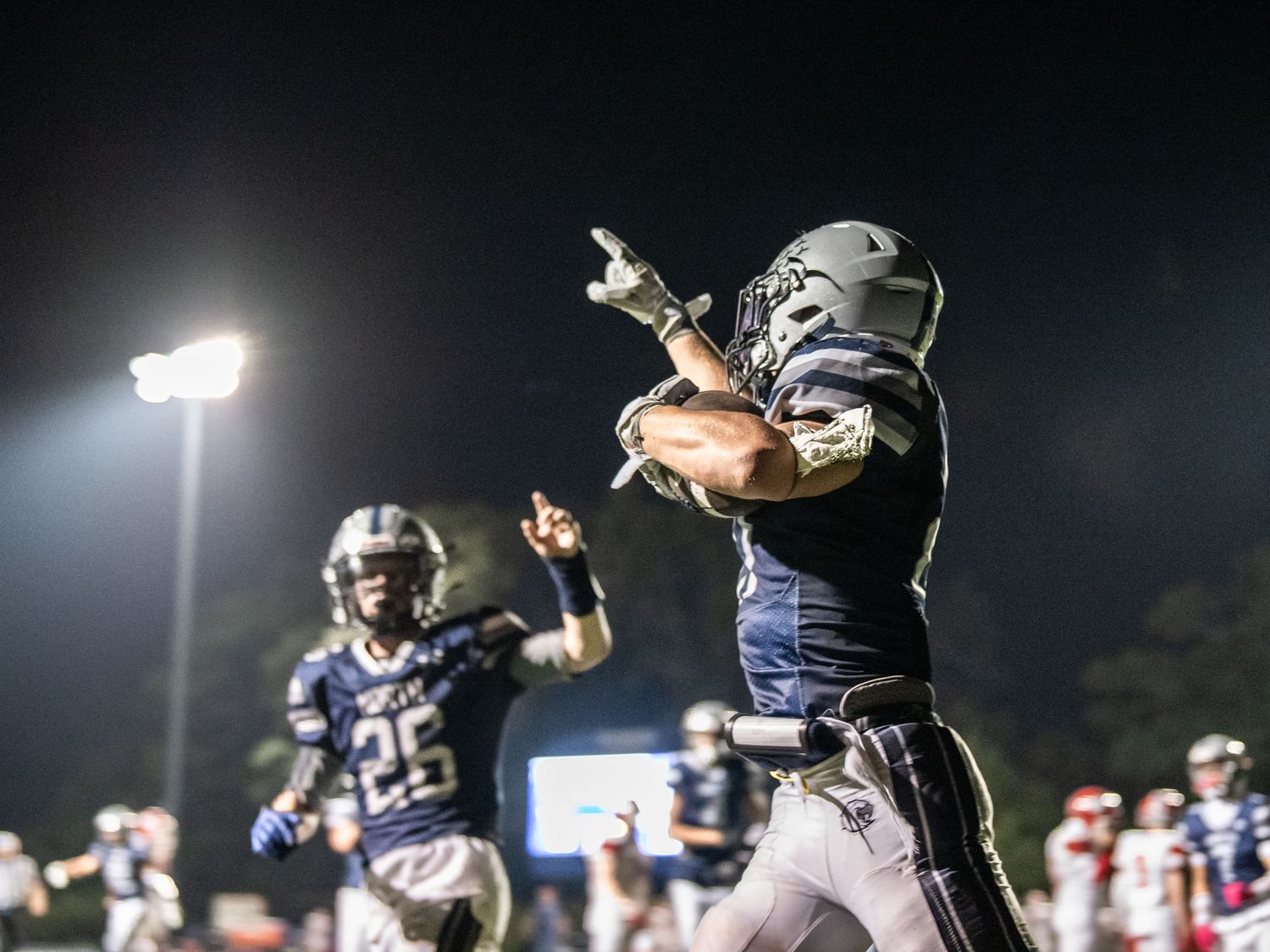 High school football player leaping to make a dramatic catch under stadium lights during a nighttime game.