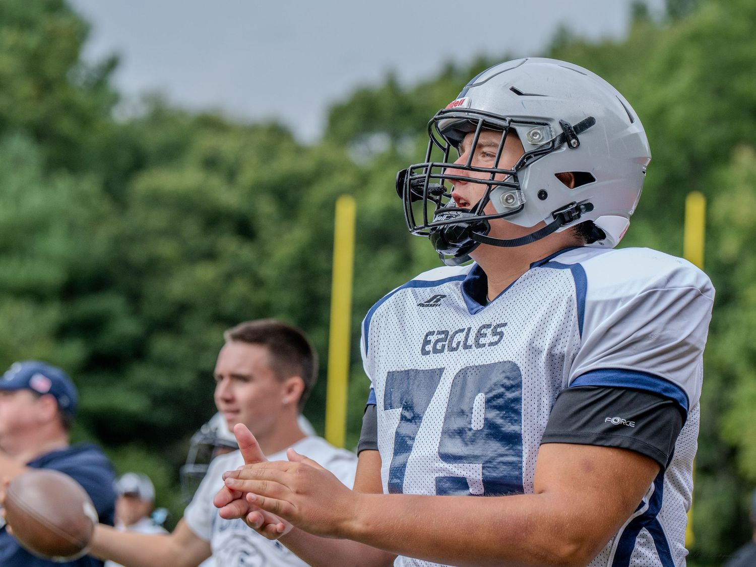 A football player in white uniform with Eagles branding stands on the sidelines.