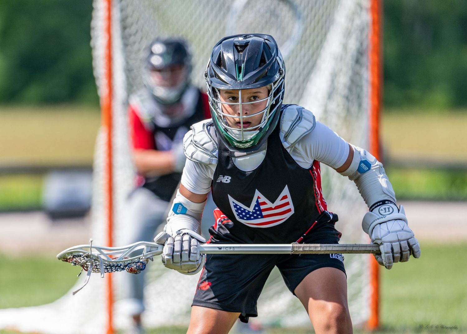 Lacrosse players in protective gear practicing on outdoor field.