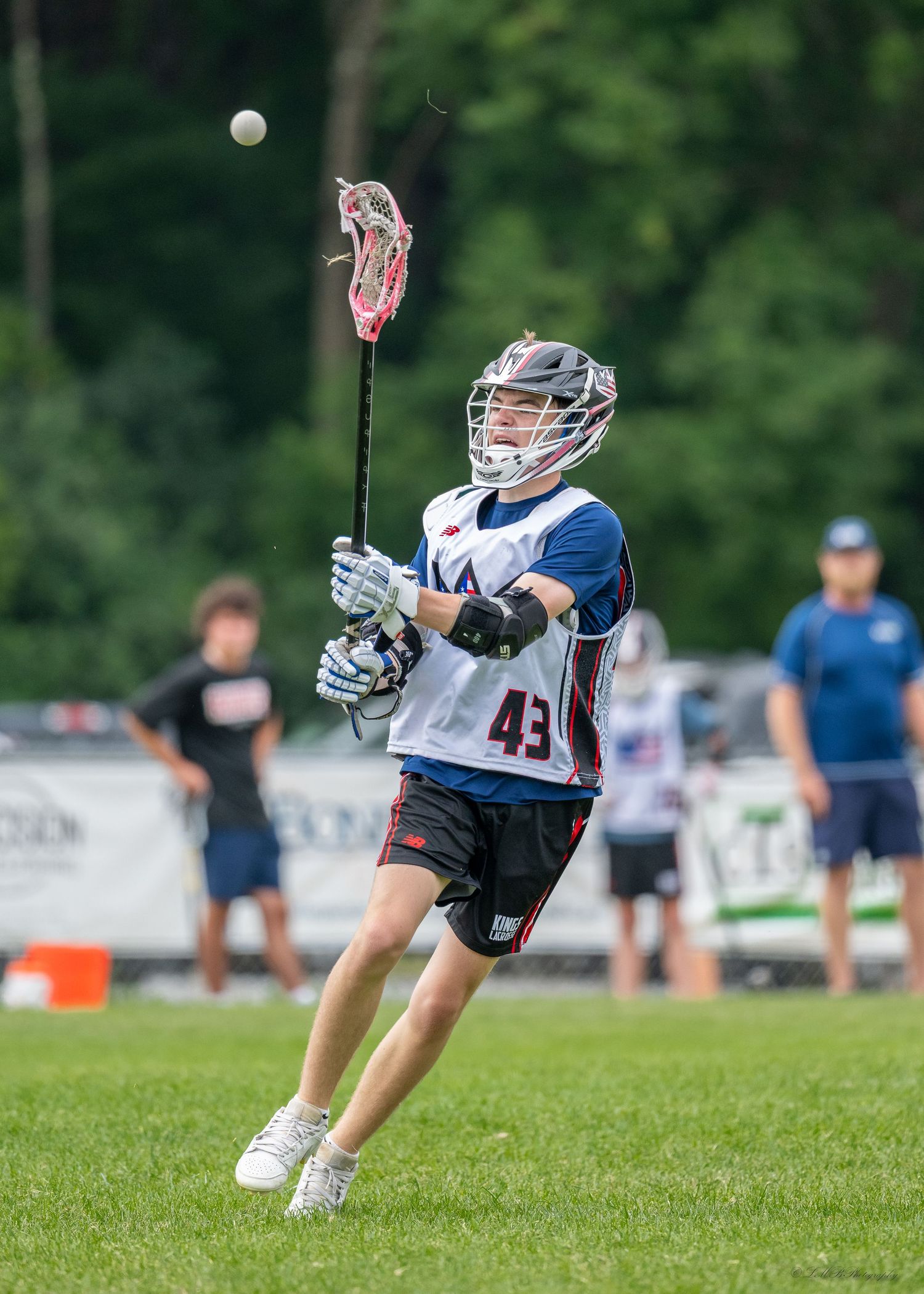 Lacrosse player in blue and white uniform scooping up ball during outdoor game action.